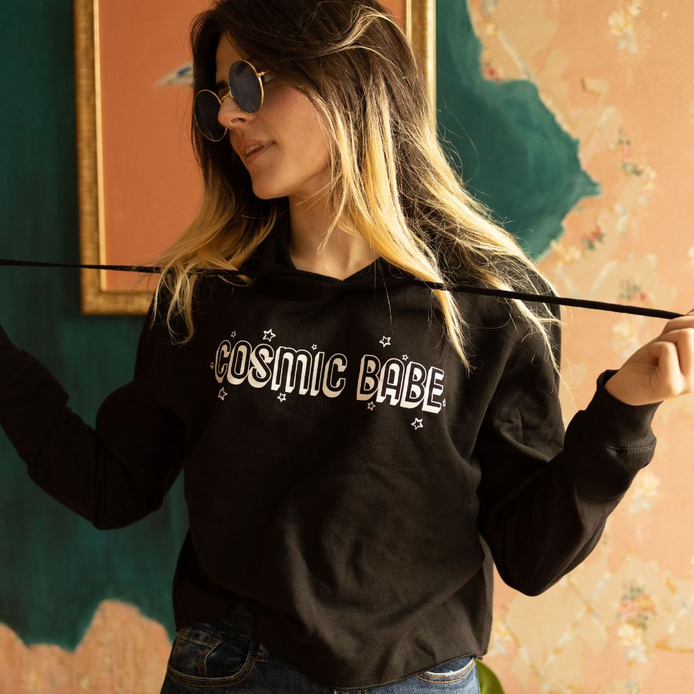 The Funnel Cake Tree “Cosmic Babe” cropped black hoodie with white retro lettering and star details, styled with jeans and sunglasses for a cozy, celestial streetwear look.