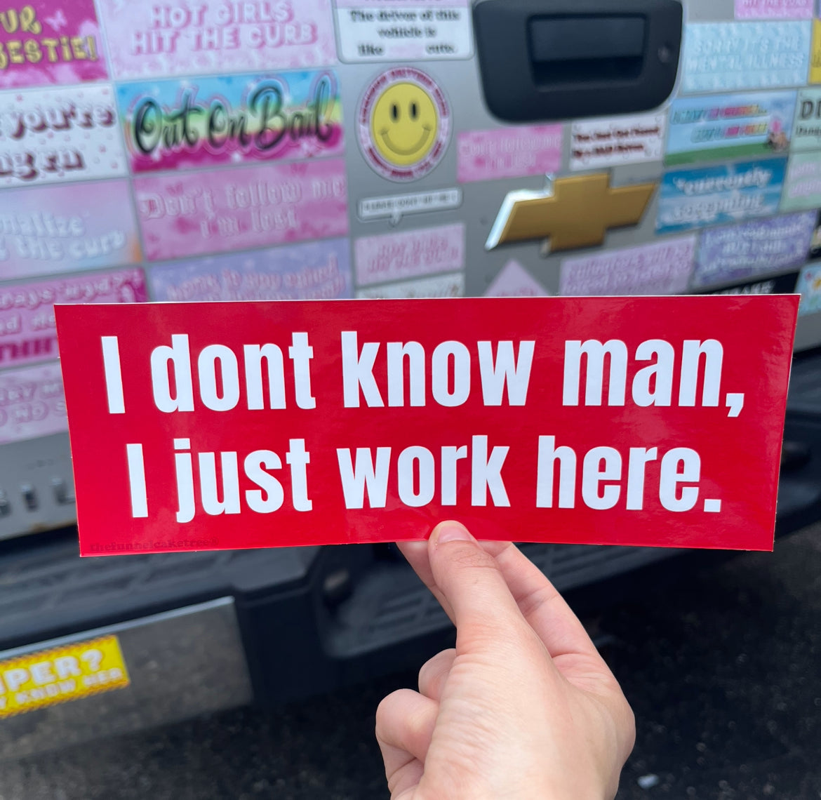 Isabel from the funnel cake tree holding a red bumper sticker that says I don't know man I just work here in white text 