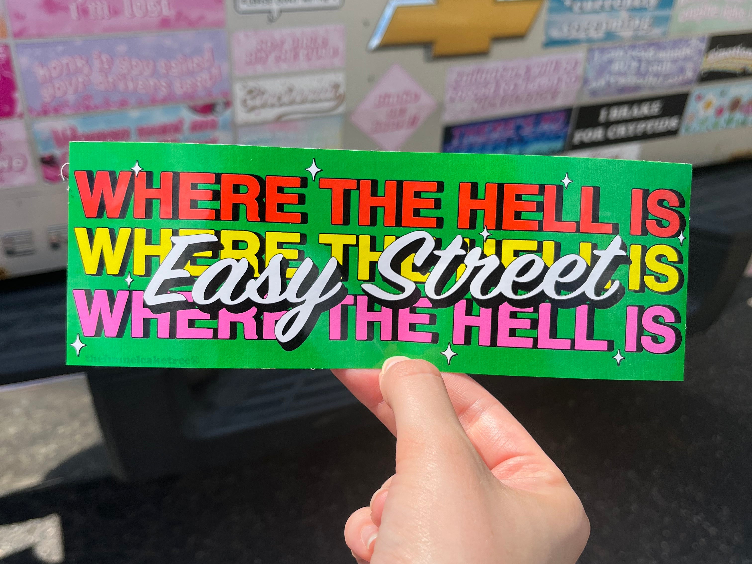 Bumper sticker with green background and red white yellow and pink text that reads where the hell is easy street 