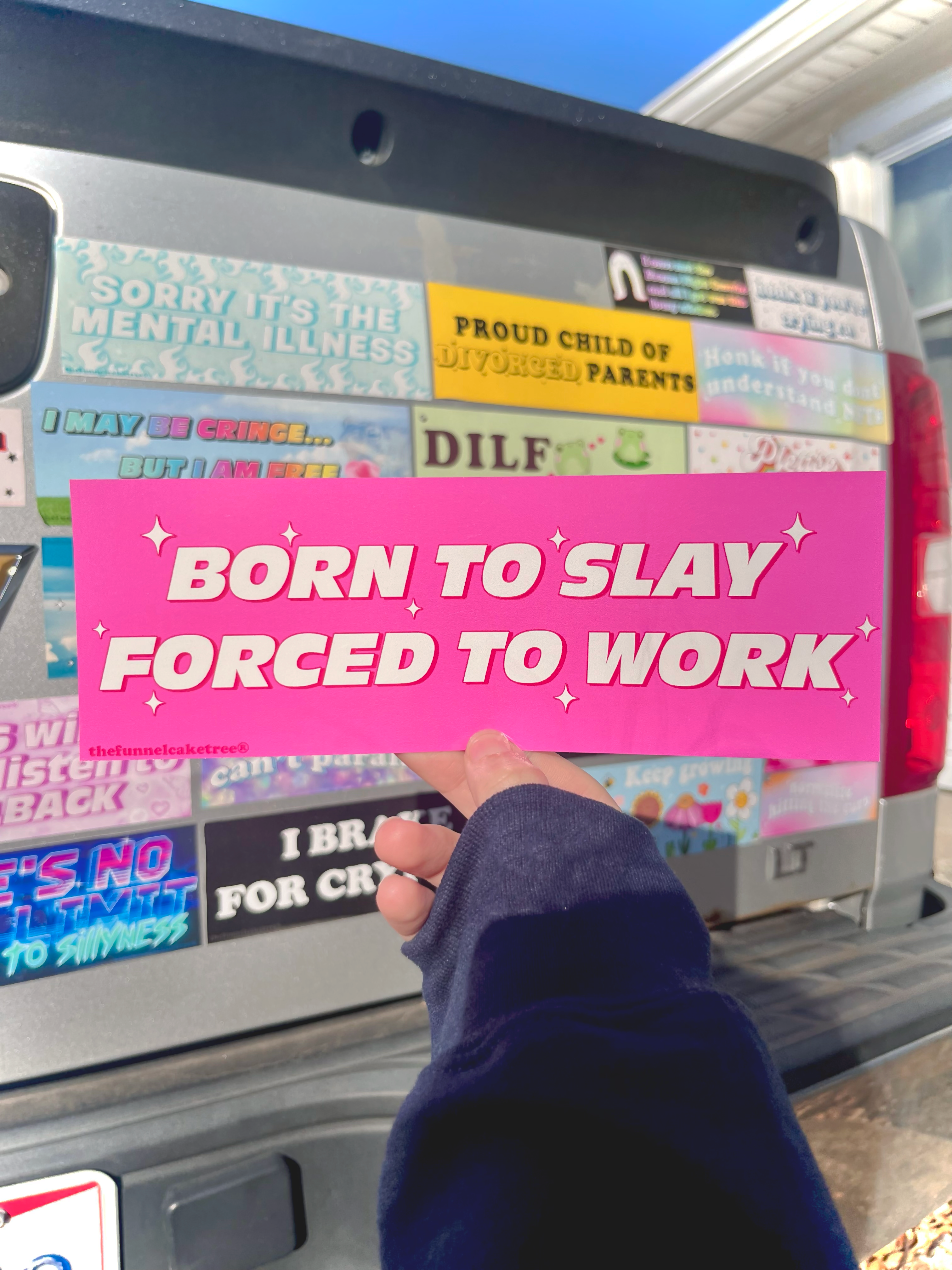 “Funny vinyl bumper sticker that says ‘Born to Slay Forced To Work’ in front of a truck— waterproof and UV-protected, perfect for cars.”