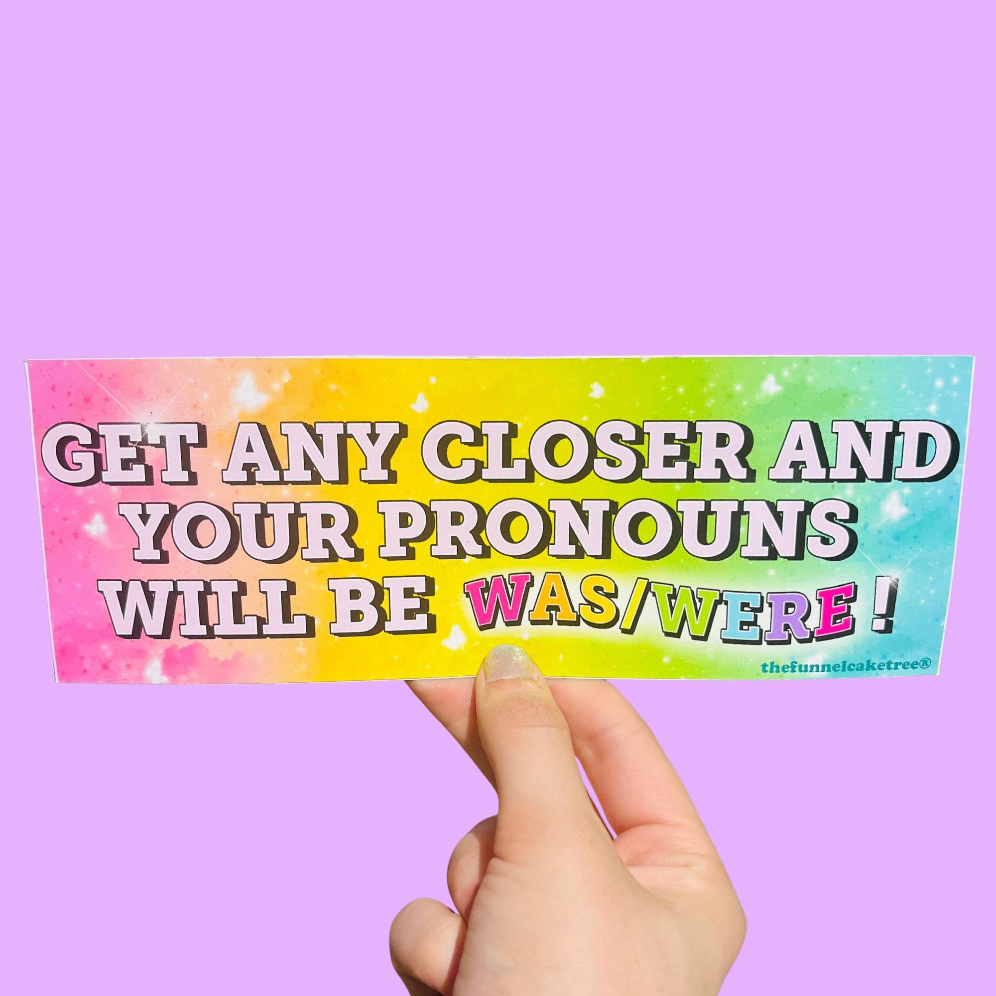  Glossy rainbow gradient bumper sticker with bold black and pink text reading “Get any closer and your pronouns will be was/were!” on a colorful splatter background.