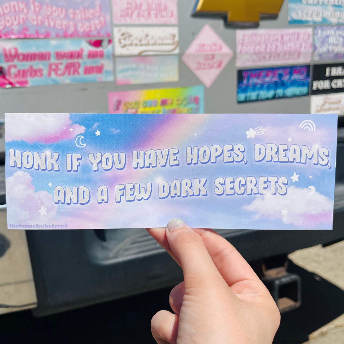 Hand holding a bumper sticker reading Honk if you have hopes dreams and a few dark secrets