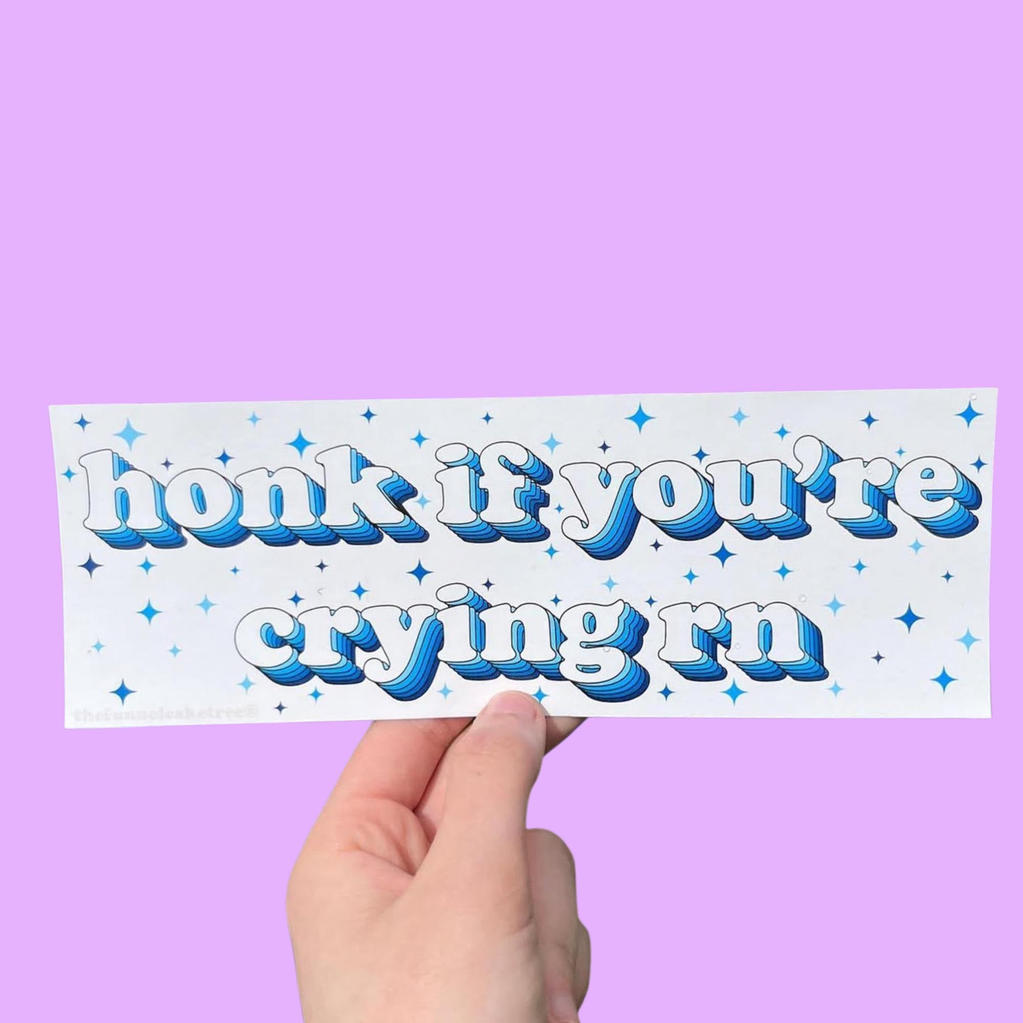 Funny vinyl bumper sticker that says ‘Honk if you're crying rn’ in blue font on a light colored background — waterproof and UV-protected, perfect for cars.