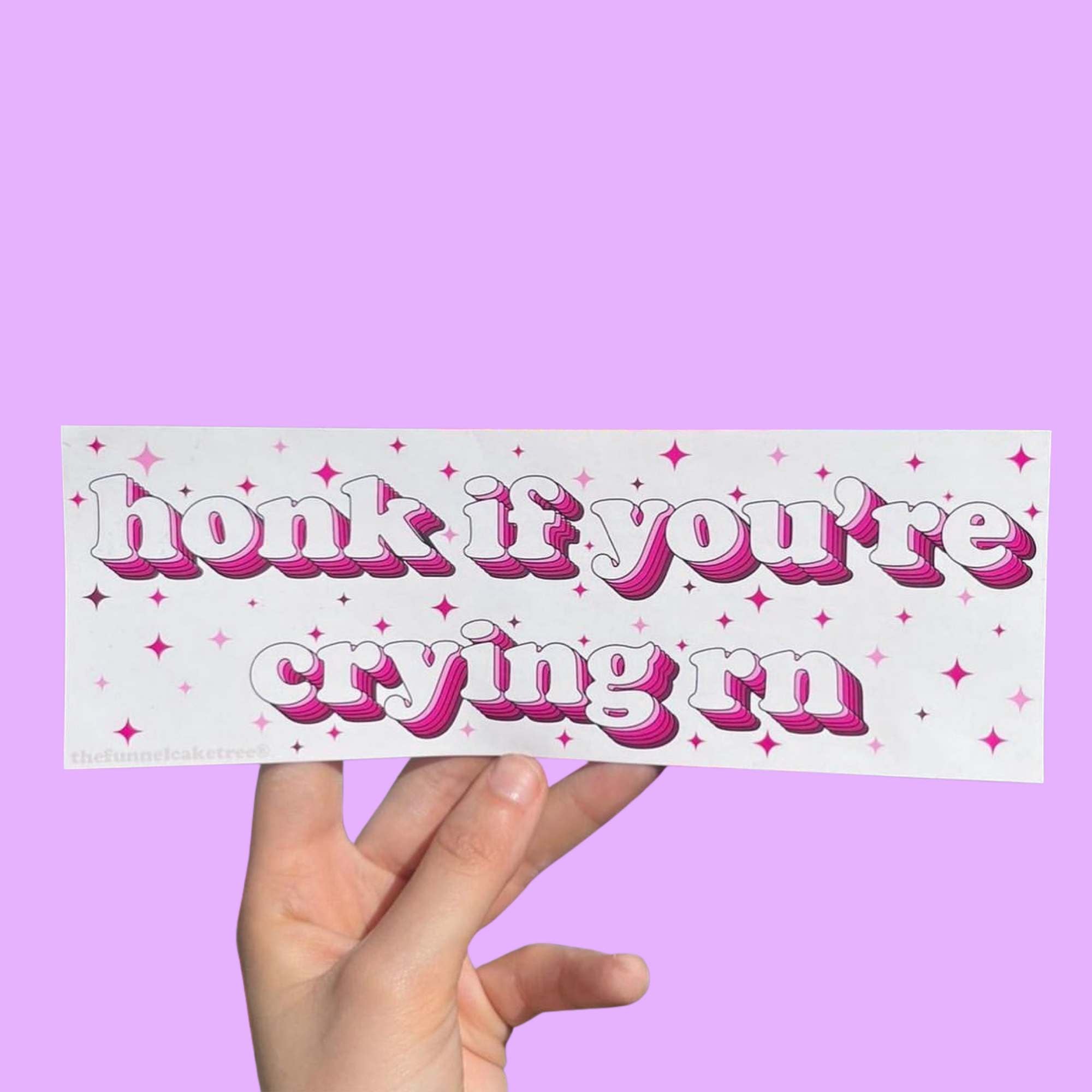 Funny vinyl bumper sticker that says ‘Honk if you're crying rn’ in pink font on a light colored background — waterproof and UV-protected, perfect for cars.