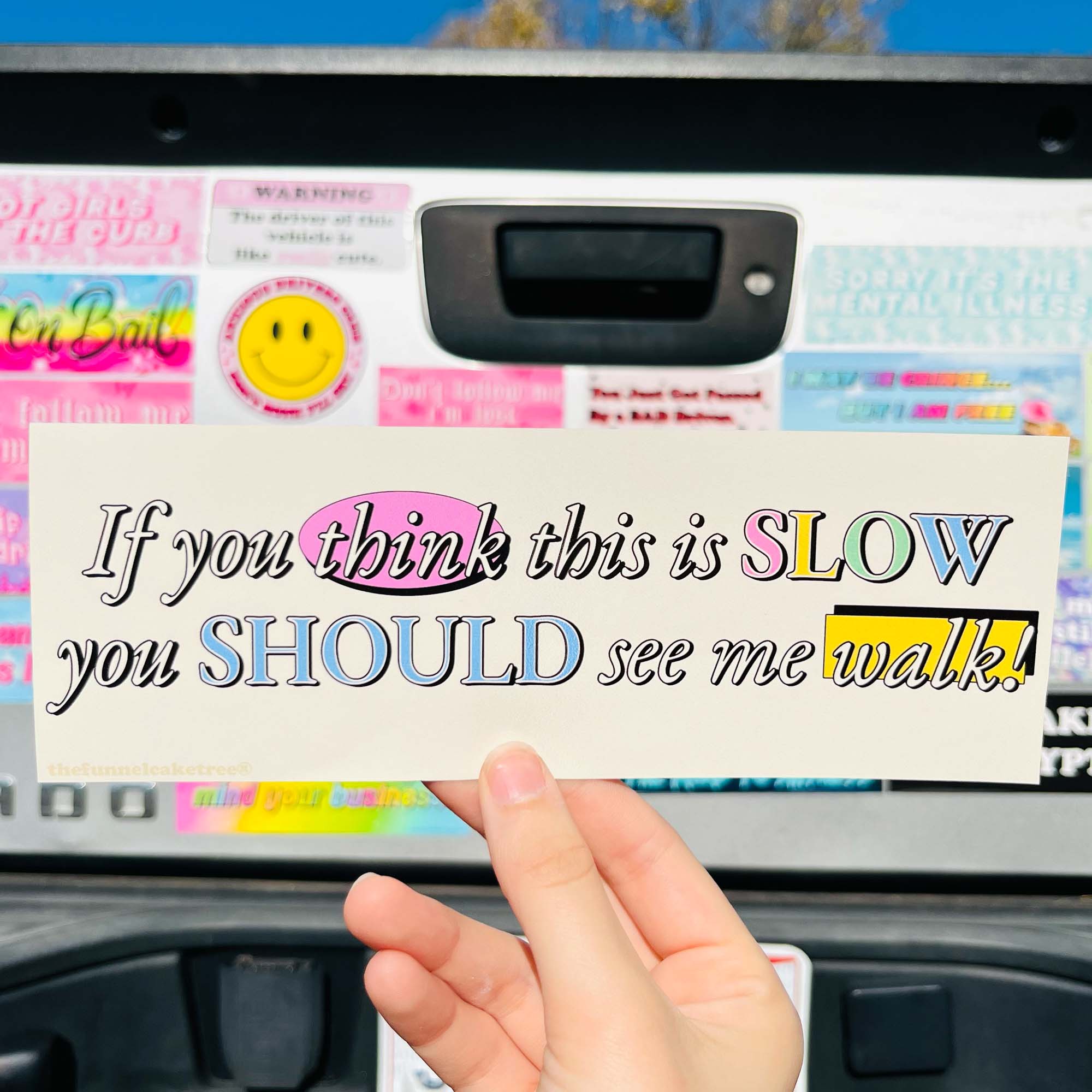 A hand placing a bumper sticker with the text 'If you think this is SLOW you SHOULD see me walk!' on a car's rear window.