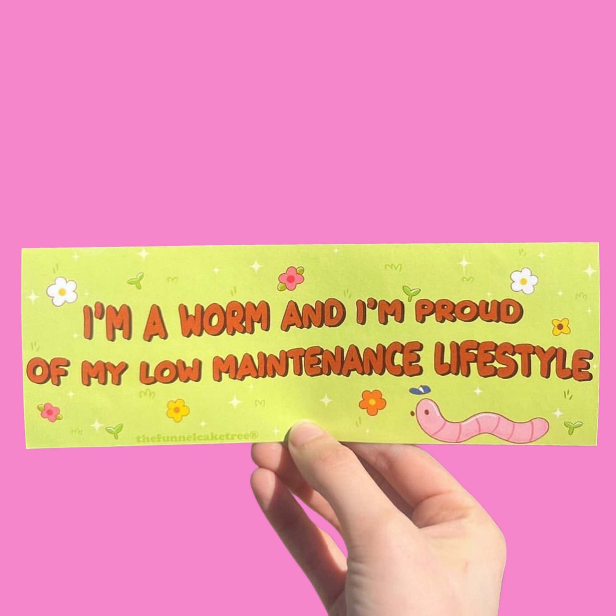  Glossy green bumper sticker with cartoon flowers and a pink worm illustration, featuring text reading “I’m a worm and I’m proud of my low maintenance lifestyle.”