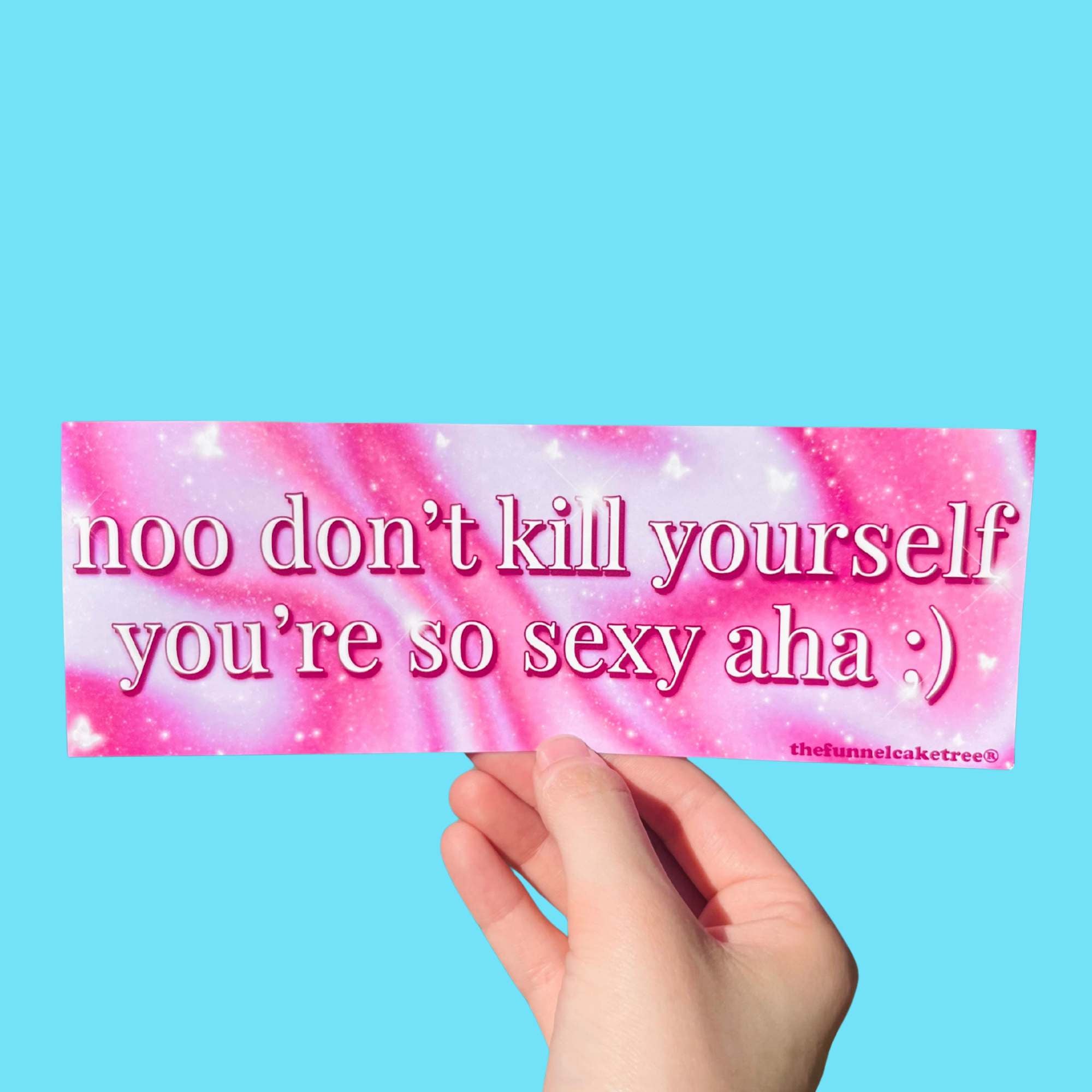 Glossy pink and white swirl bumper sticker with text reading “noo don’t kill yourself you’re so sexy aha :)” held against a blue background.