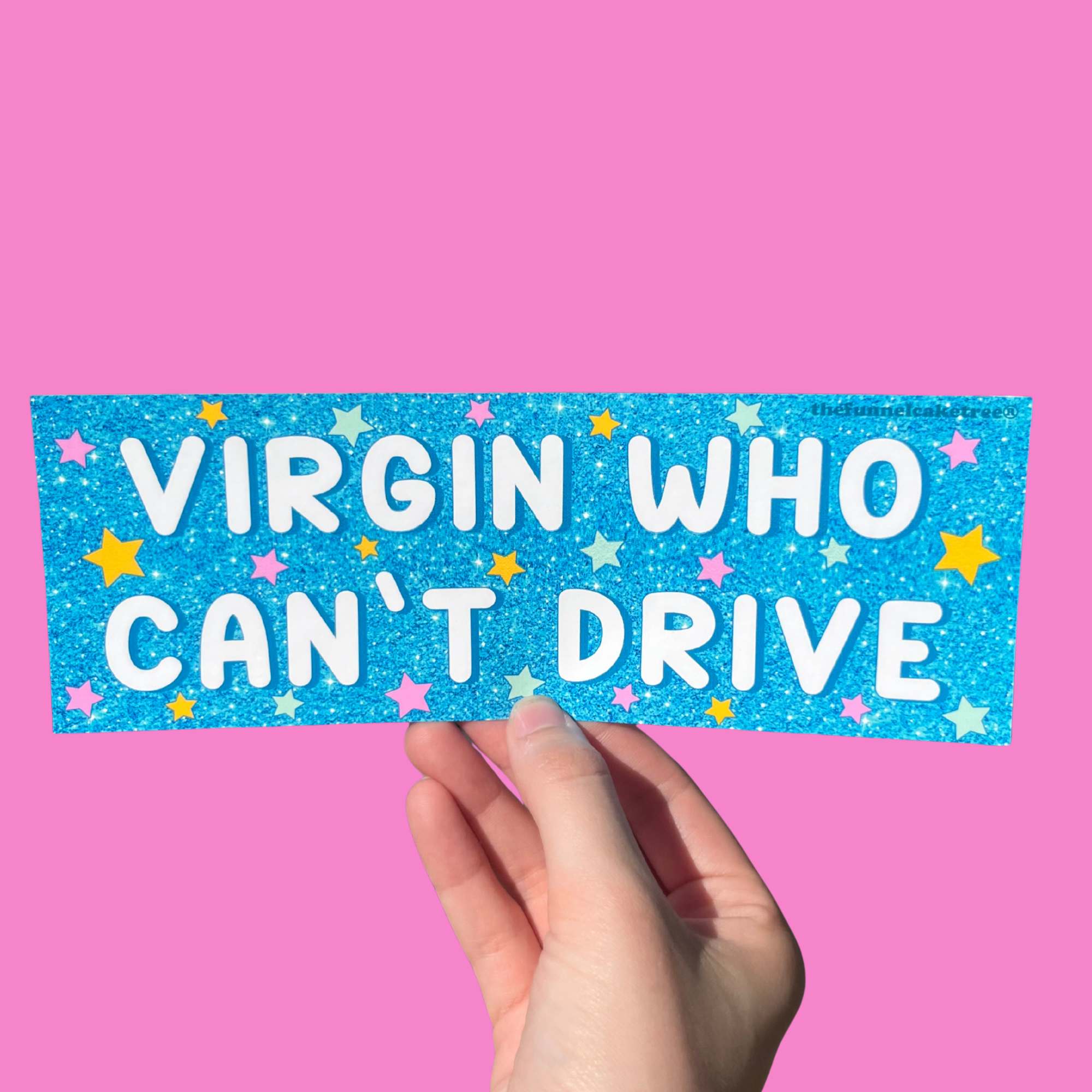 Glossy blue glitter bumper sticker with colorful stars and bold white text reading “VIRGIN WHO CAN’T DRIVE,” held against a pink background.