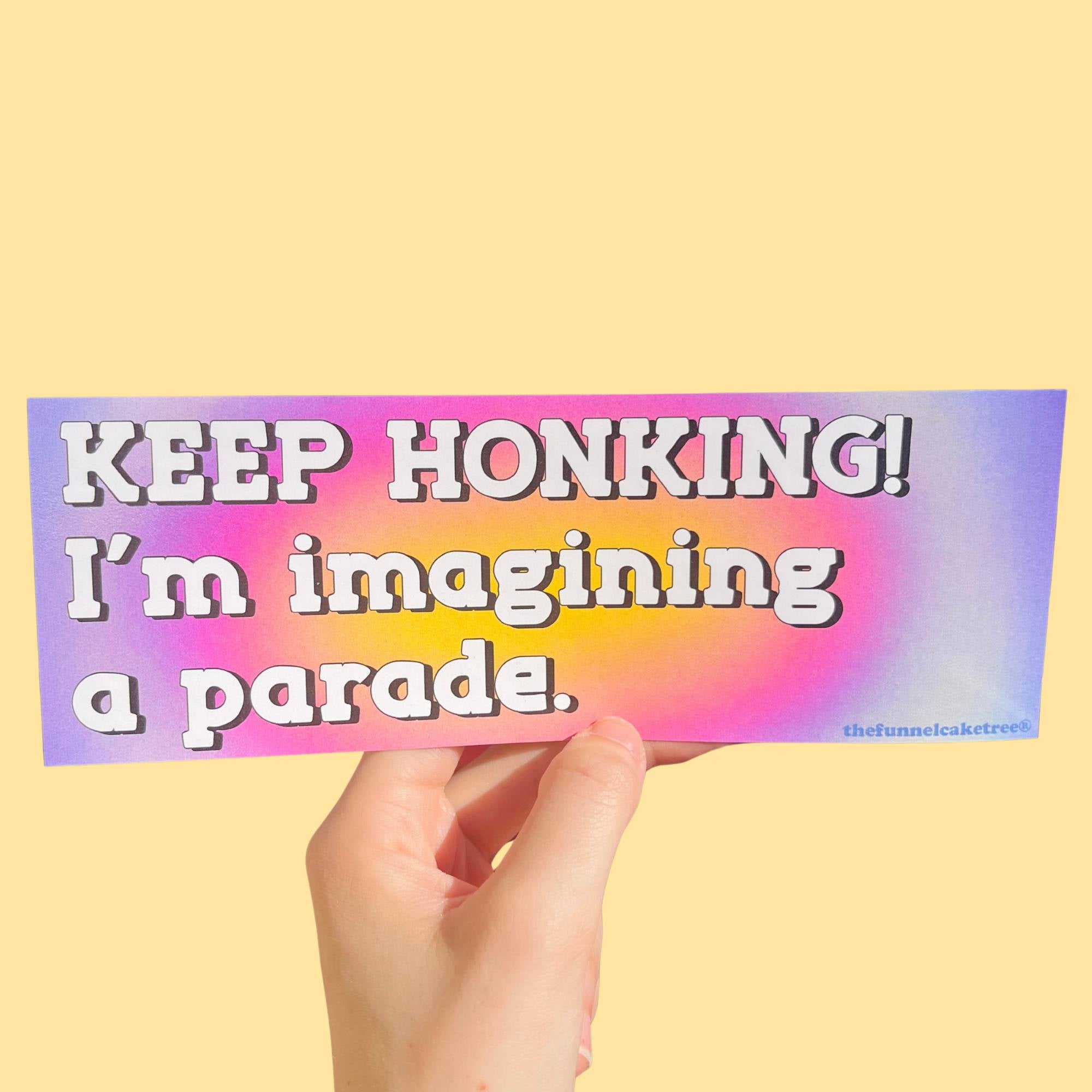 Glossy gradient bumper sticker with pink, purple, and yellow background and white text reading “Keep honking! I’m imagining a parade.”
