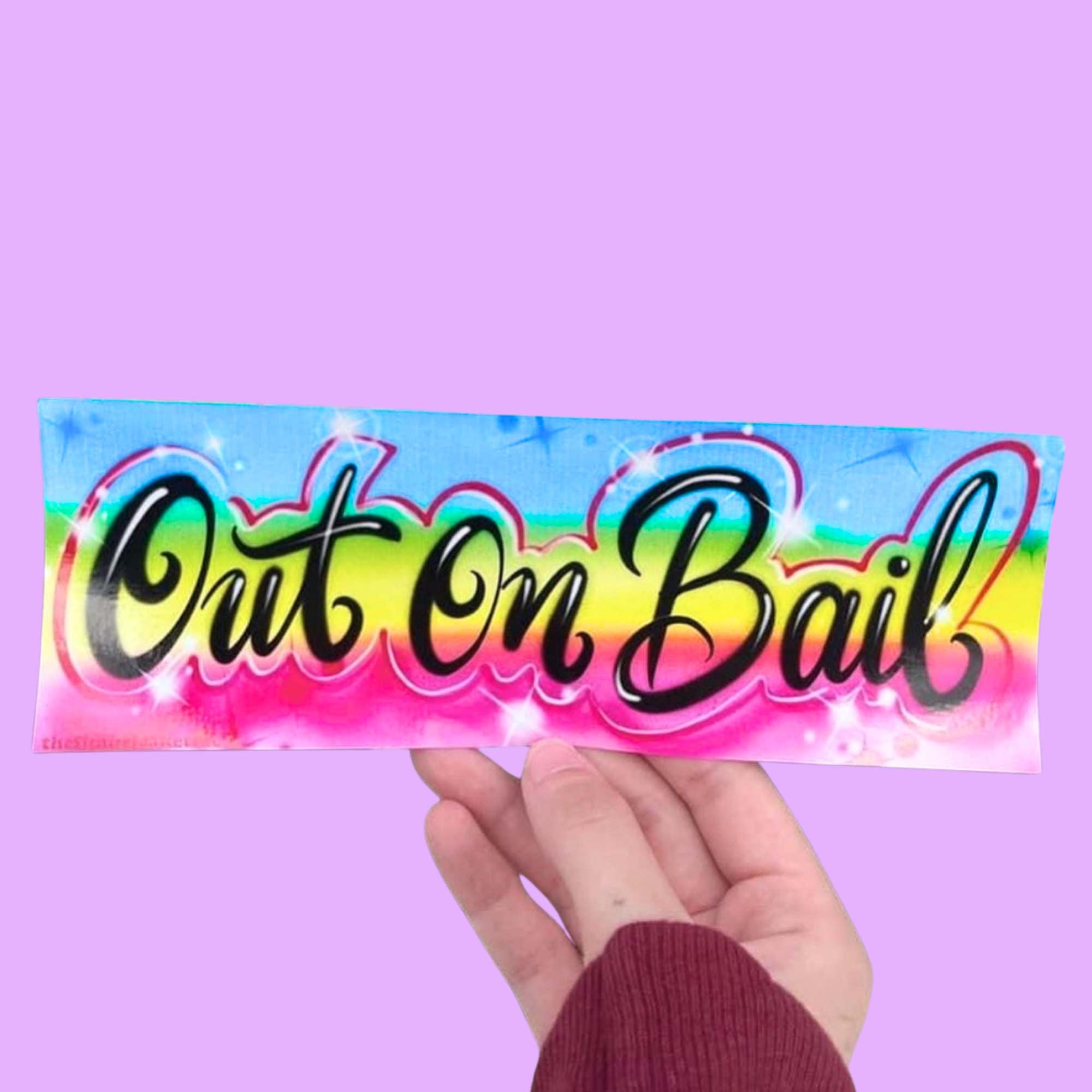  “Funny vinyl bumper sticker that says ‘Out on Bail’ in front of a purple background — waterproof and UV-protected, perfect for cars.”
 