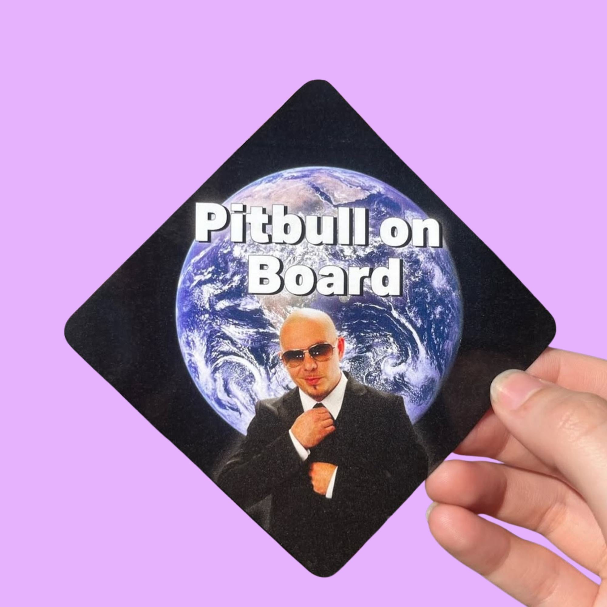 Glossy black diamond-shaped sticker with image of Pitbull in a suit in front of Earth and white text reading “Pitbull on Board,” held against a lavender background.