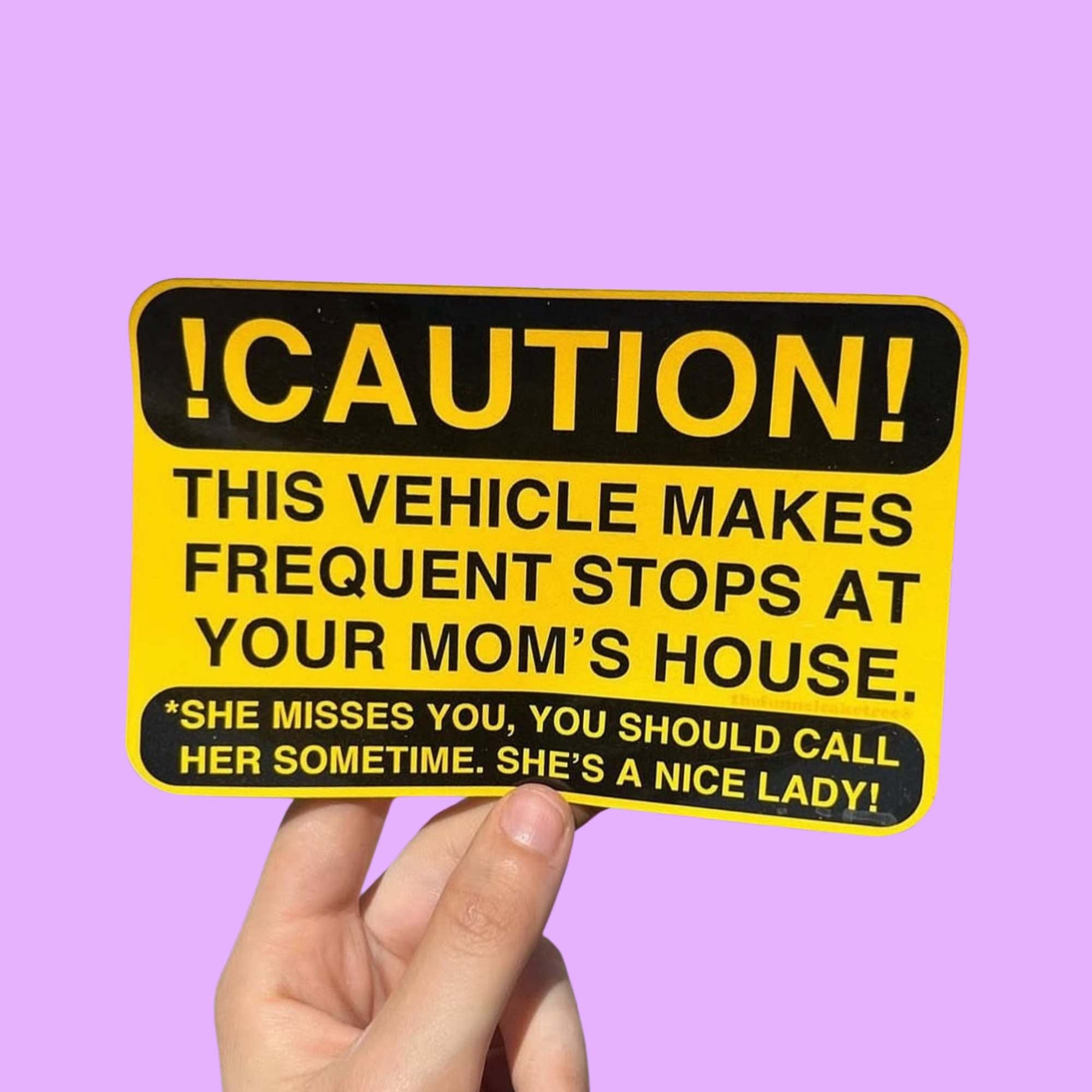 Glossy yellow and black caution-style bumper sticker reading “CAUTION! This vehicle makes frequent stops at your mom’s house,” with smaller text that says “She misses you, you should call her sometime. She’s a nice lady!”