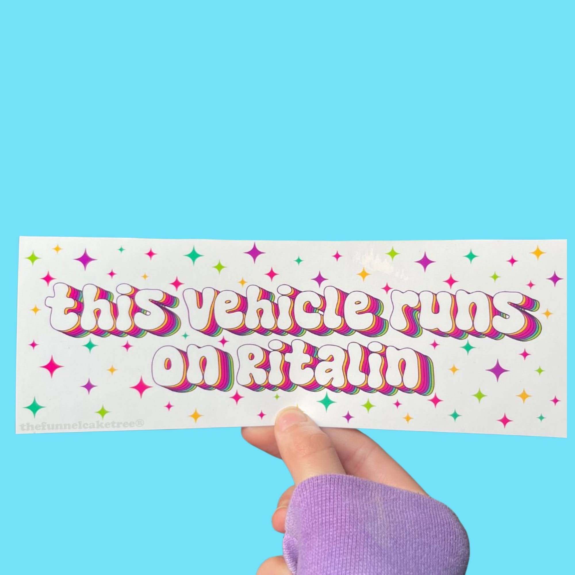 Glossy white bumper sticker with colorful rainbow-outlined text reading “This vehicle runs on Ritalin,” surrounded by bright star accents.
