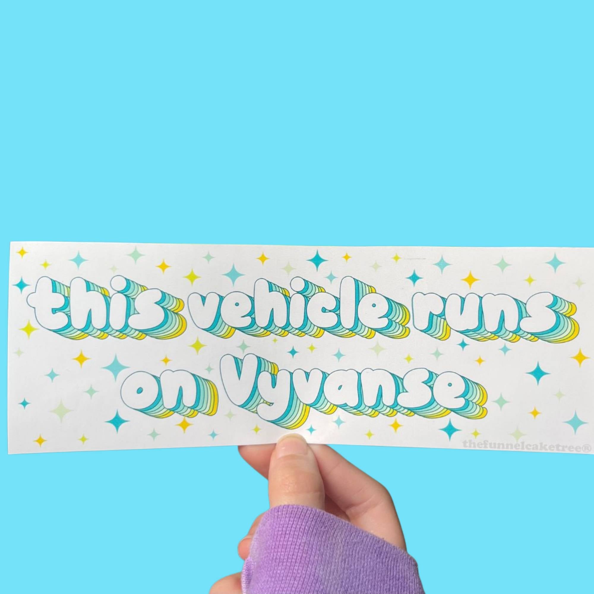 Glossy white bumper sticker with teal and yellow text reading “This vehicle runs on Vyvanse,” surrounded by colorful starburst accents.