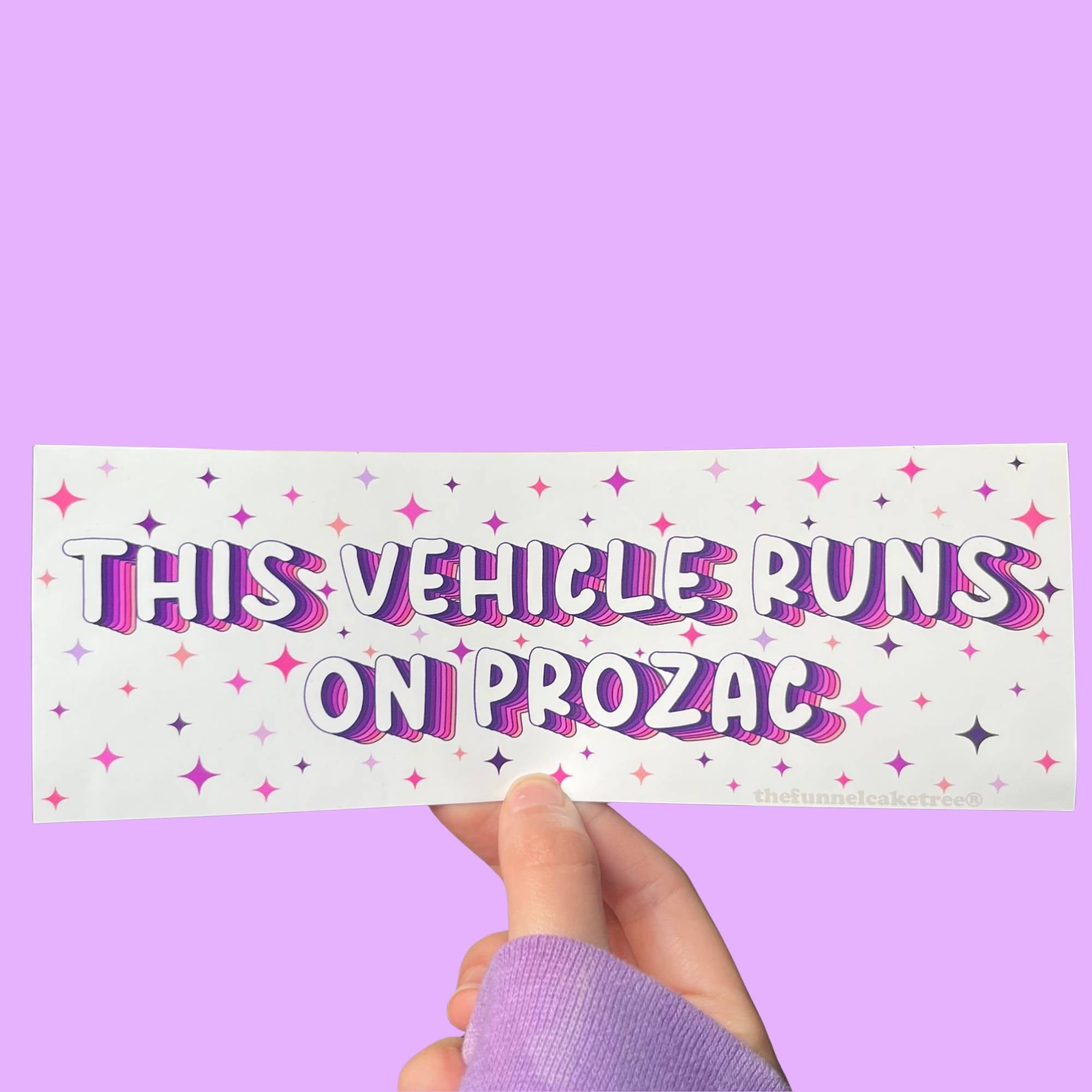  Glossy white bumper sticker with purple and pink text reading “This vehicle runs on Prozac,” surrounded by colorful starburst accents.