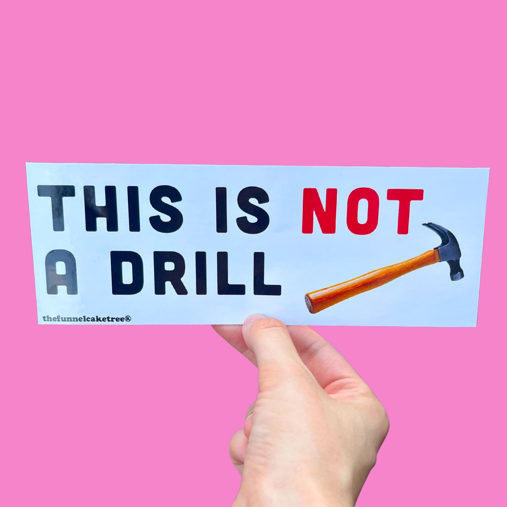 Glossy white bumper sticker with bold black and red text reading “This Is Not a Drill” next to an illustrated hammer.