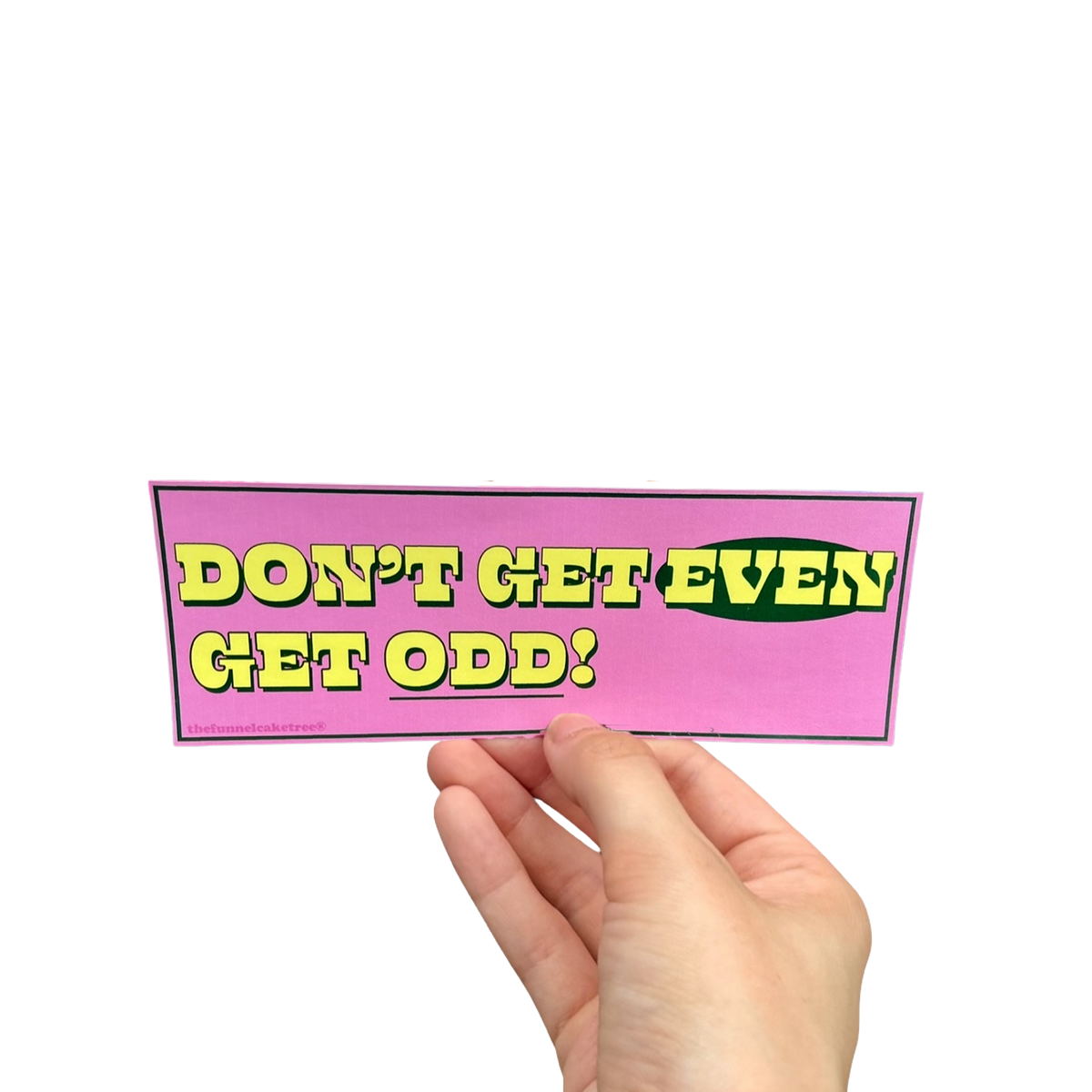 Hand holding a pink mini bumper sticker reading 'Don't get even! Get odd!' in yellow and green lettering.