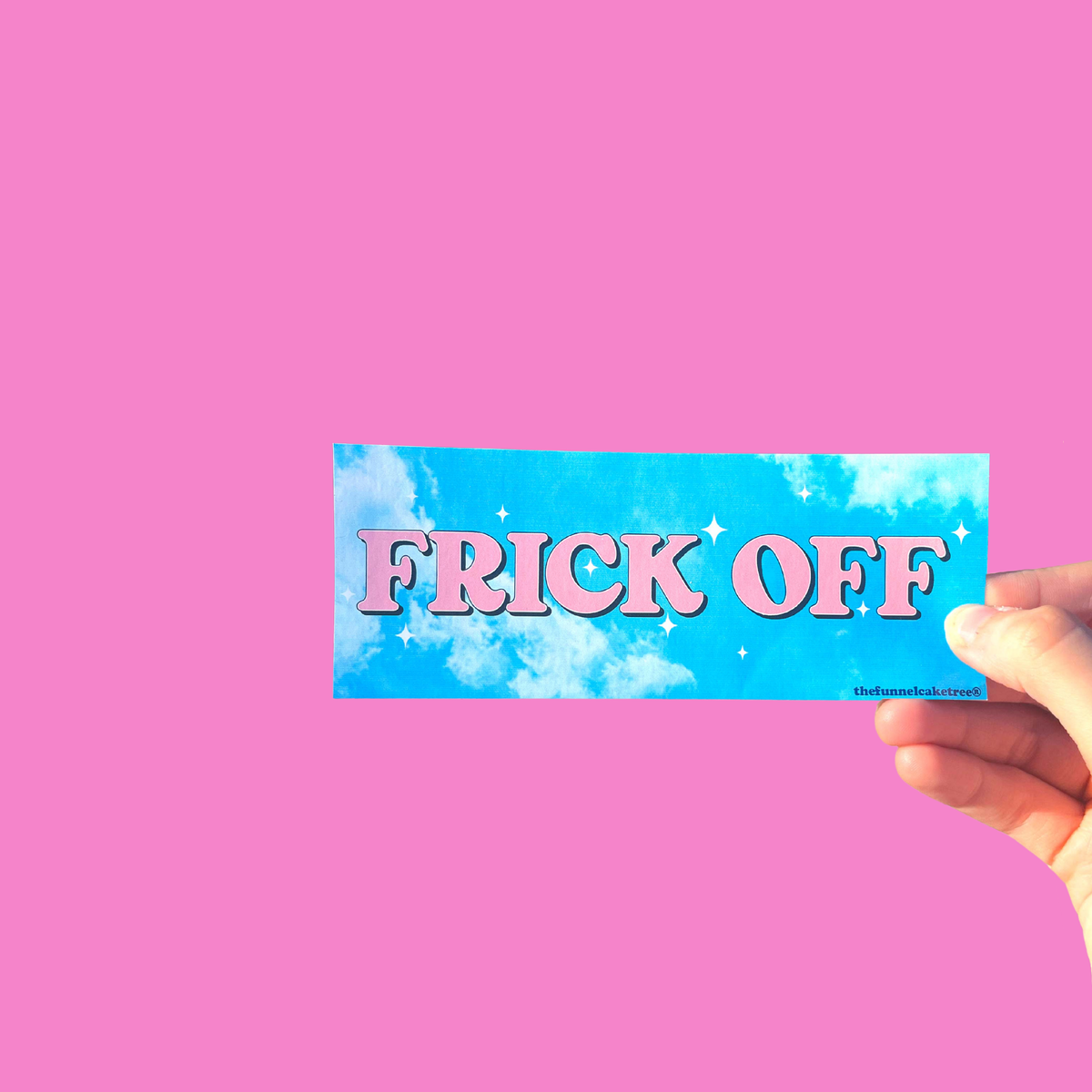 Hand holding a blue mini bumper sticker reading 'FRICK OFF' in pink lettering On a solid pink background.