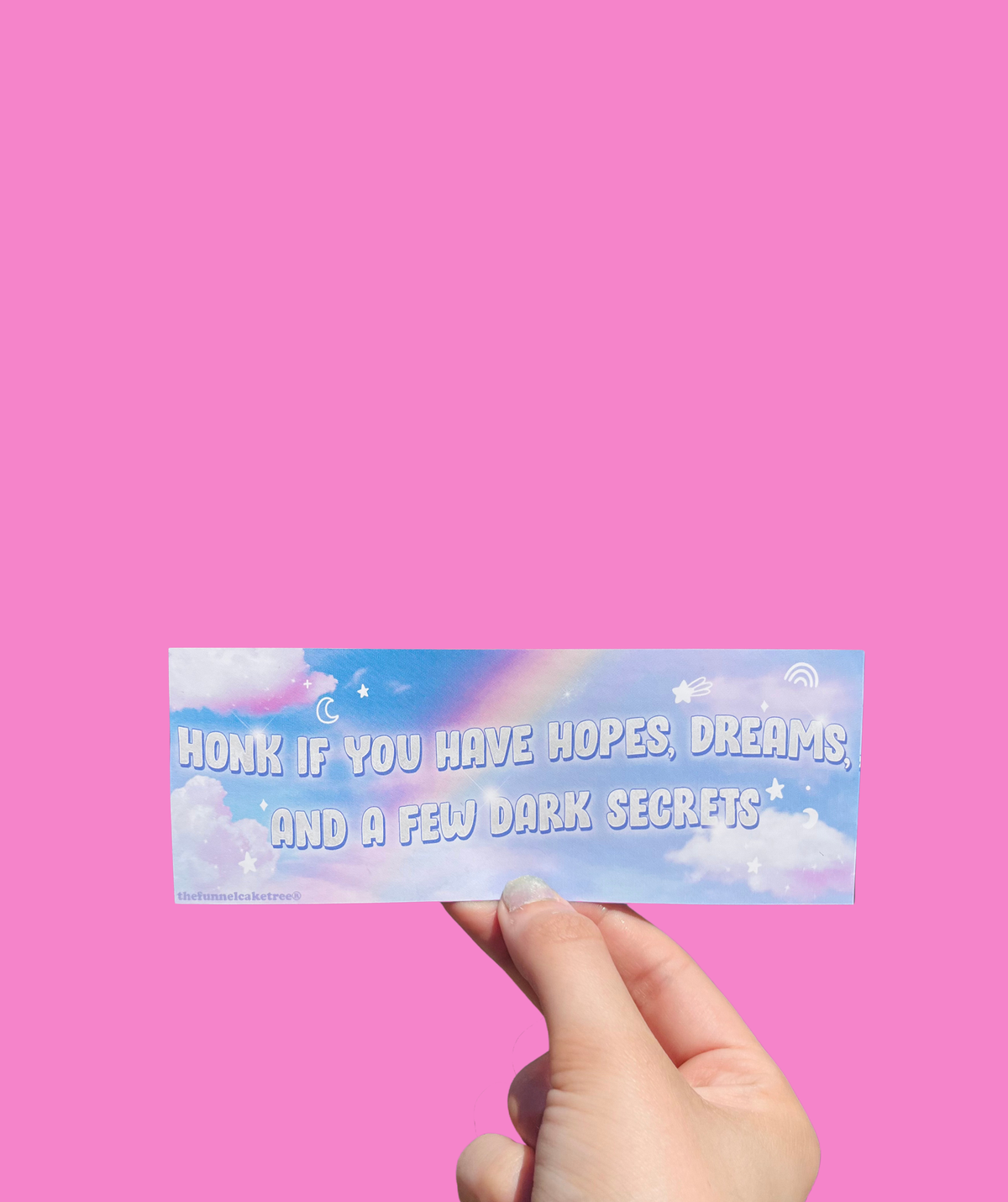 Hand holding a cloudy pastel mini sticker reading 'Honk if you have hopes, dreams and a few dark secrets.' On a solid pink background.