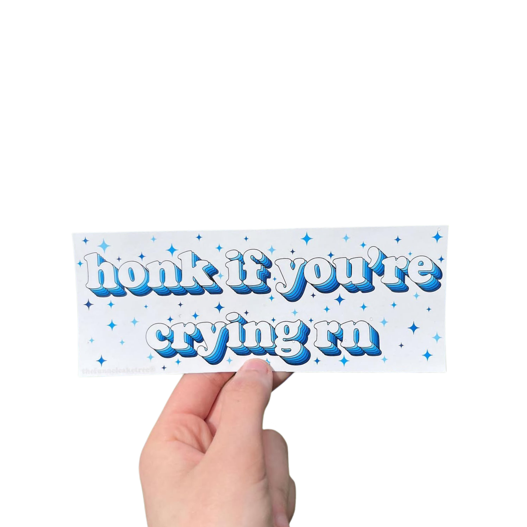 Hand holding a white mini bumper sticker reading 'honk if you're crying rn' in blue lettering with stars.