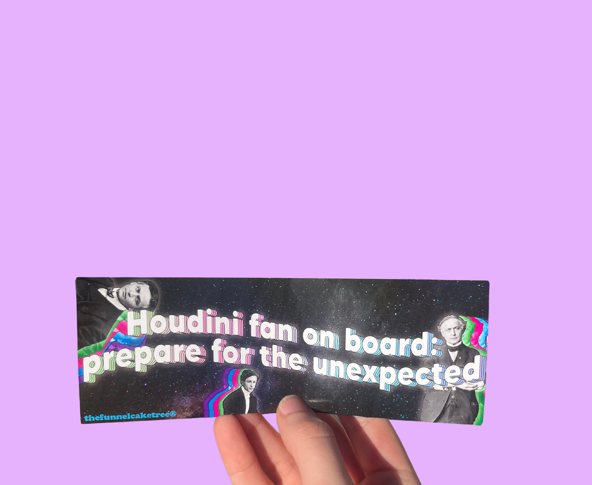 Hand holding a black 'Houdini fan on board: prepare for the unexpected' mini sticker with magician portraits On a solid purple background.