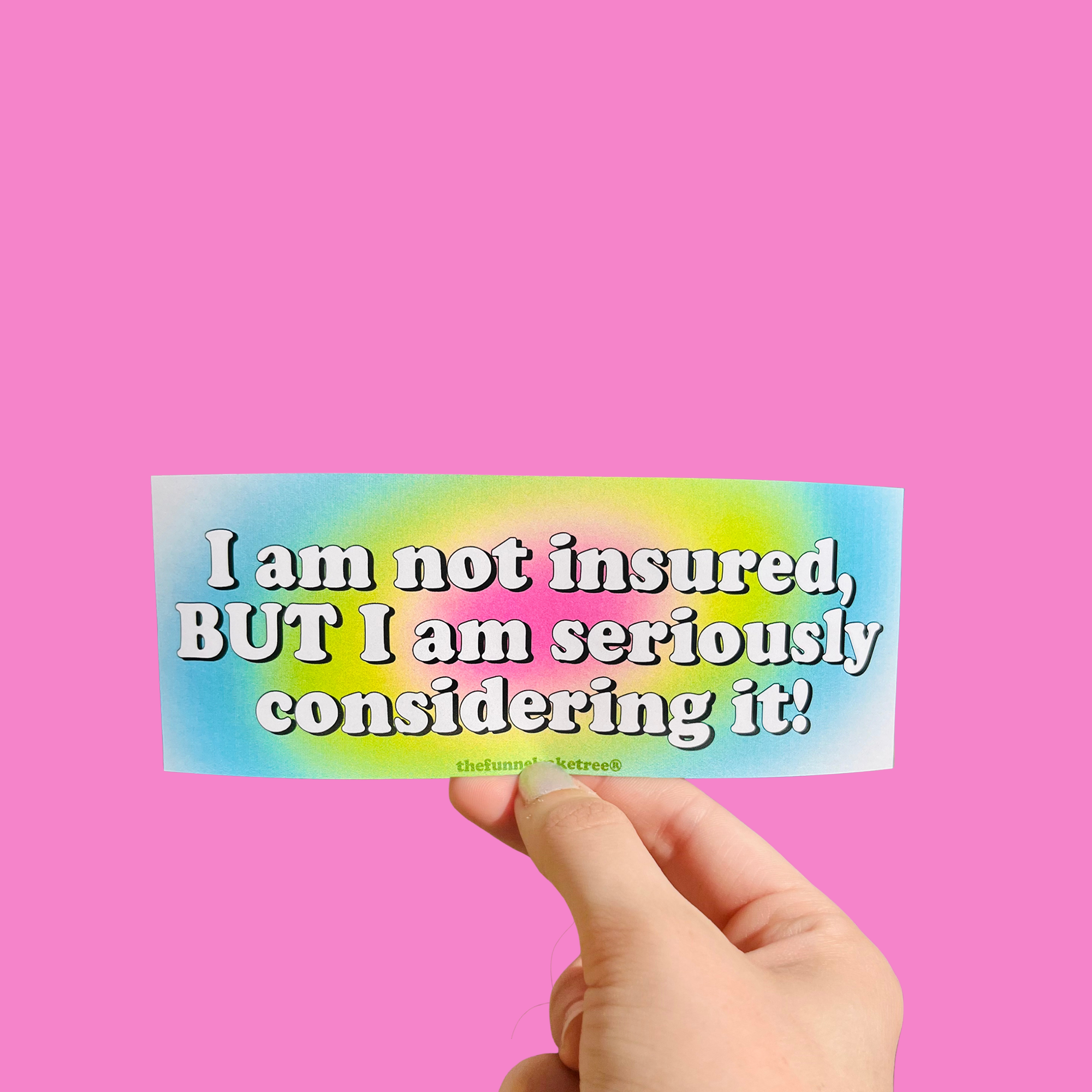 Hand holding a mini bumper sticker reading "i am not insured." On a solid pink background.