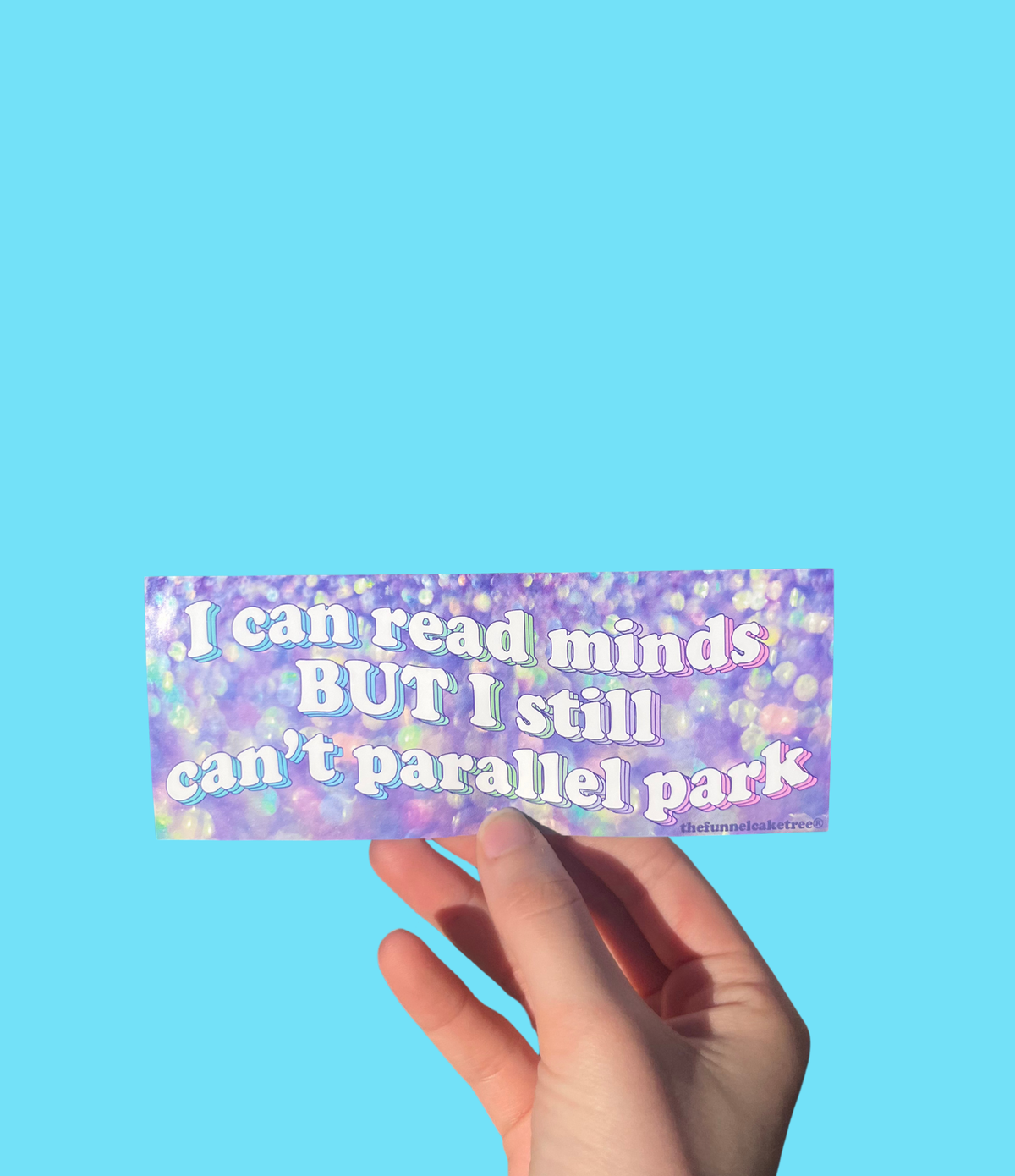 Hand holding a purple iridescent mini bumper sticker reading 'I can read minds BUT I still can't parallel park' On a solid teal background.