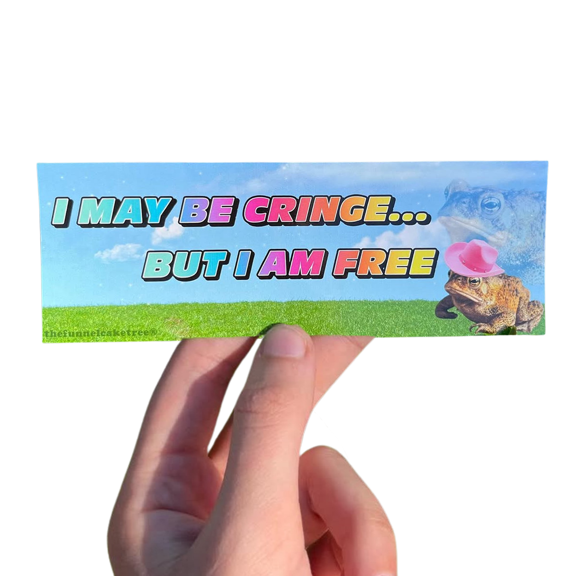 Hand holding a blue-sky mini sticker reading 'I may be cringe... but I am free,' with a frog blowing a pink bubble.