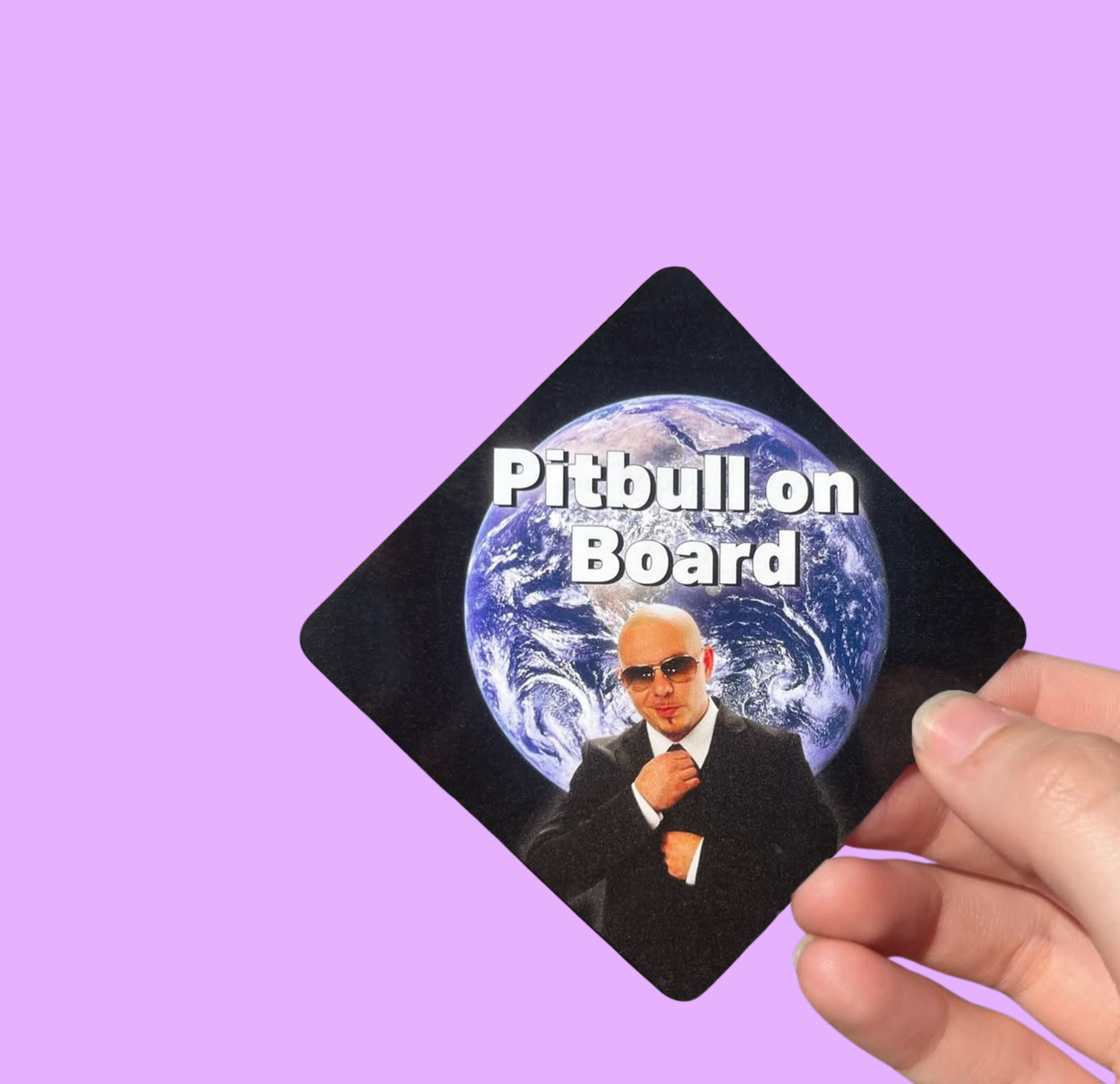 Hand holding a mini bumper sticker reading "pitbull on board." On a solid purple background.