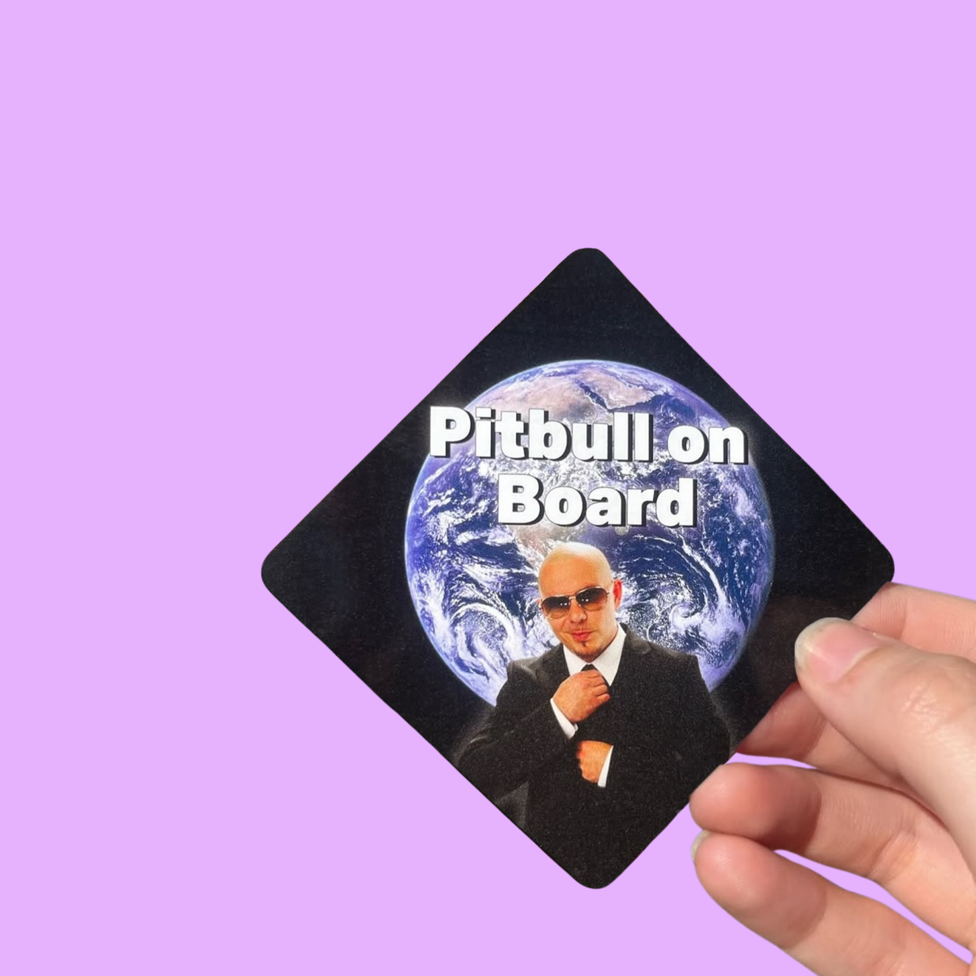 Hand holding a mini bumper sticker reading "pitbull on board." On a solid purple background.