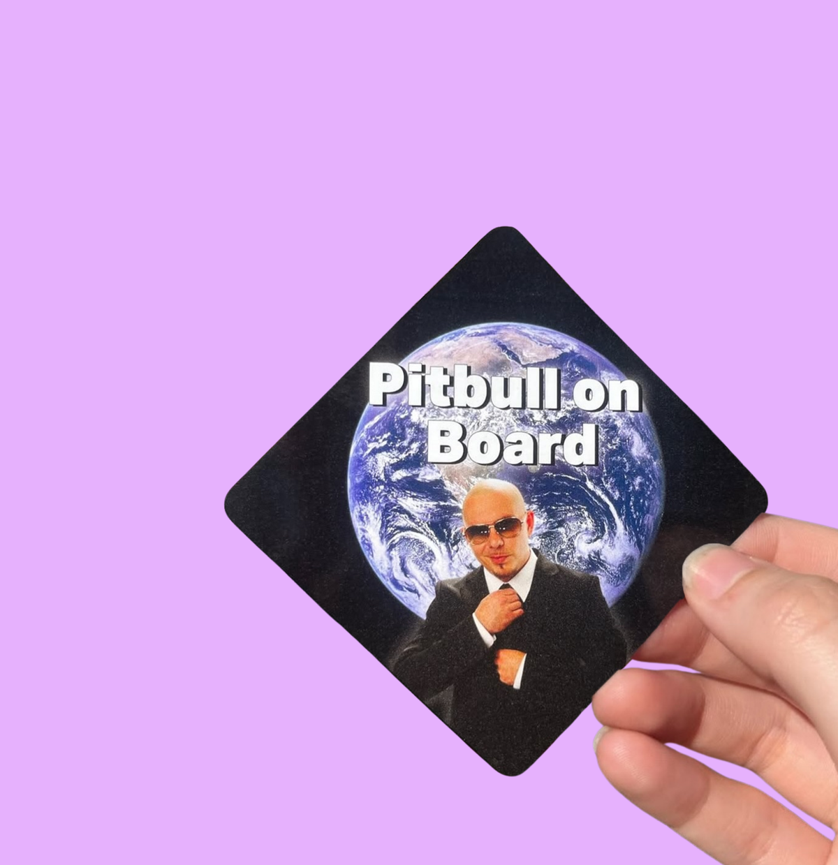 Hand holding a mini bumper sticker reading "pitbull on board." On a solid purple background.