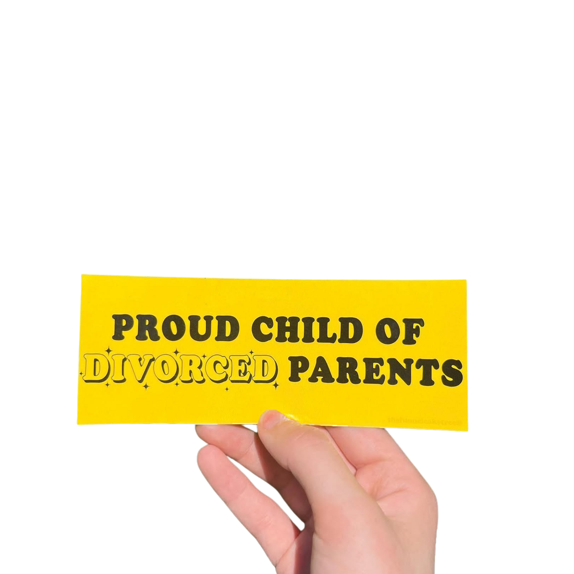 Hand holding a yellow mini bumper sticker reading 'Proud child of divorced parents' in black lettering.