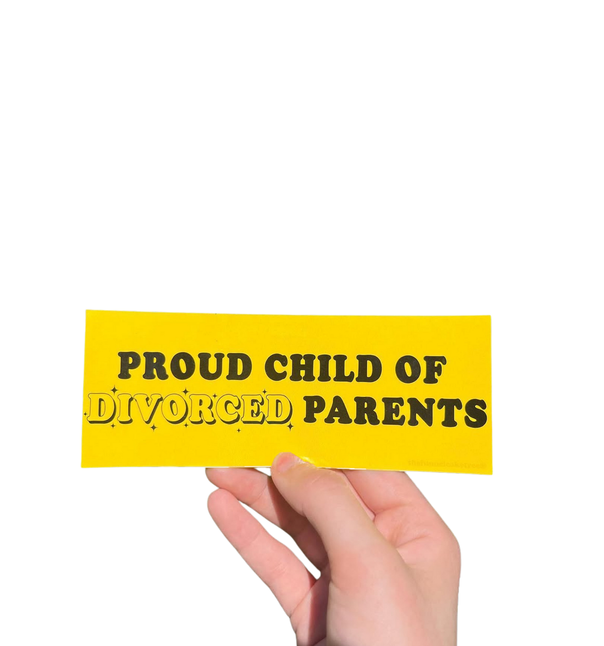 Hand holding a yellow mini bumper sticker reading 'Proud child of divorced parents' in black lettering.
