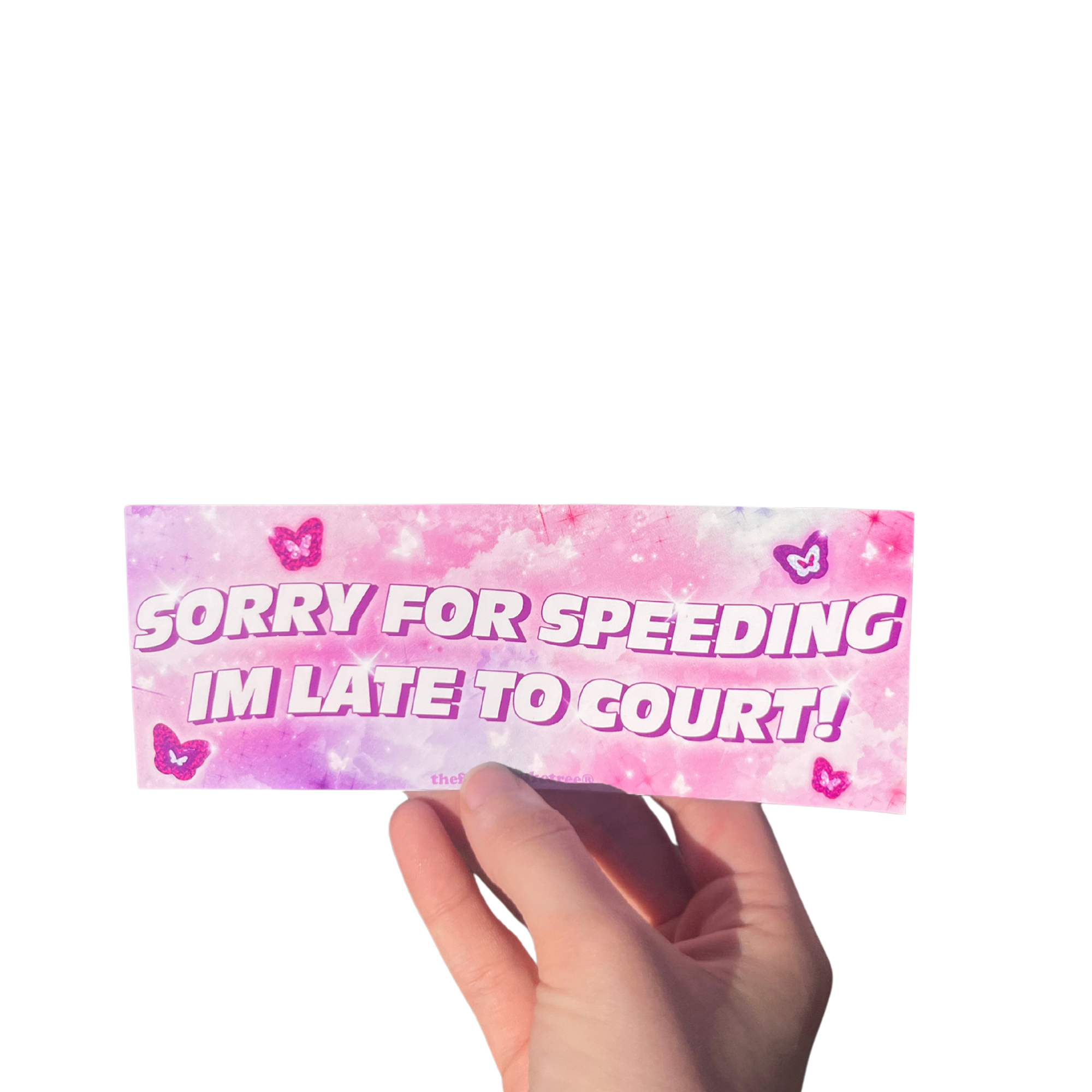 Hand holding a pink mini bumper sticker reading 'Sorry for speeding I'm late to court!' with hearts.