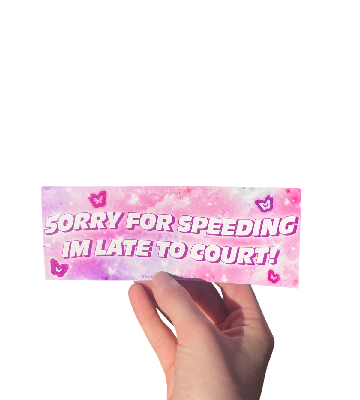 Hand holding a pink mini bumper sticker reading 'Sorry for speeding I'm late to court!' with hearts.