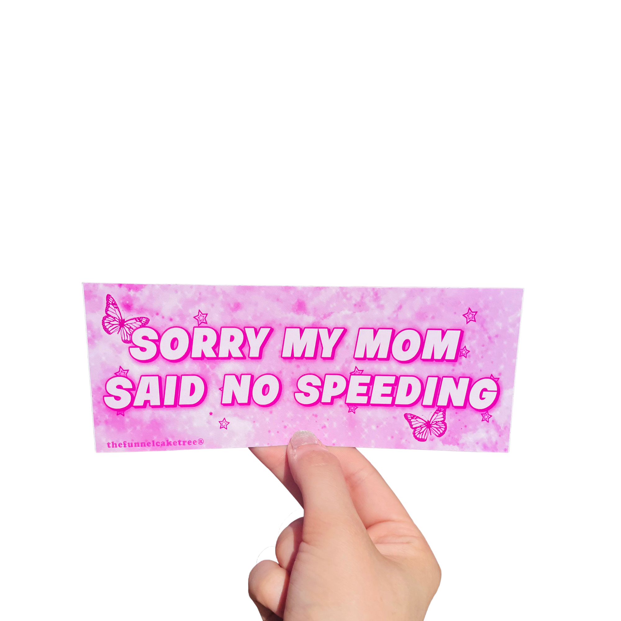 Hand holding a hot-pink mini bumper sticker reading 'Sorry my mom said no speeding' with butterflies and stars.