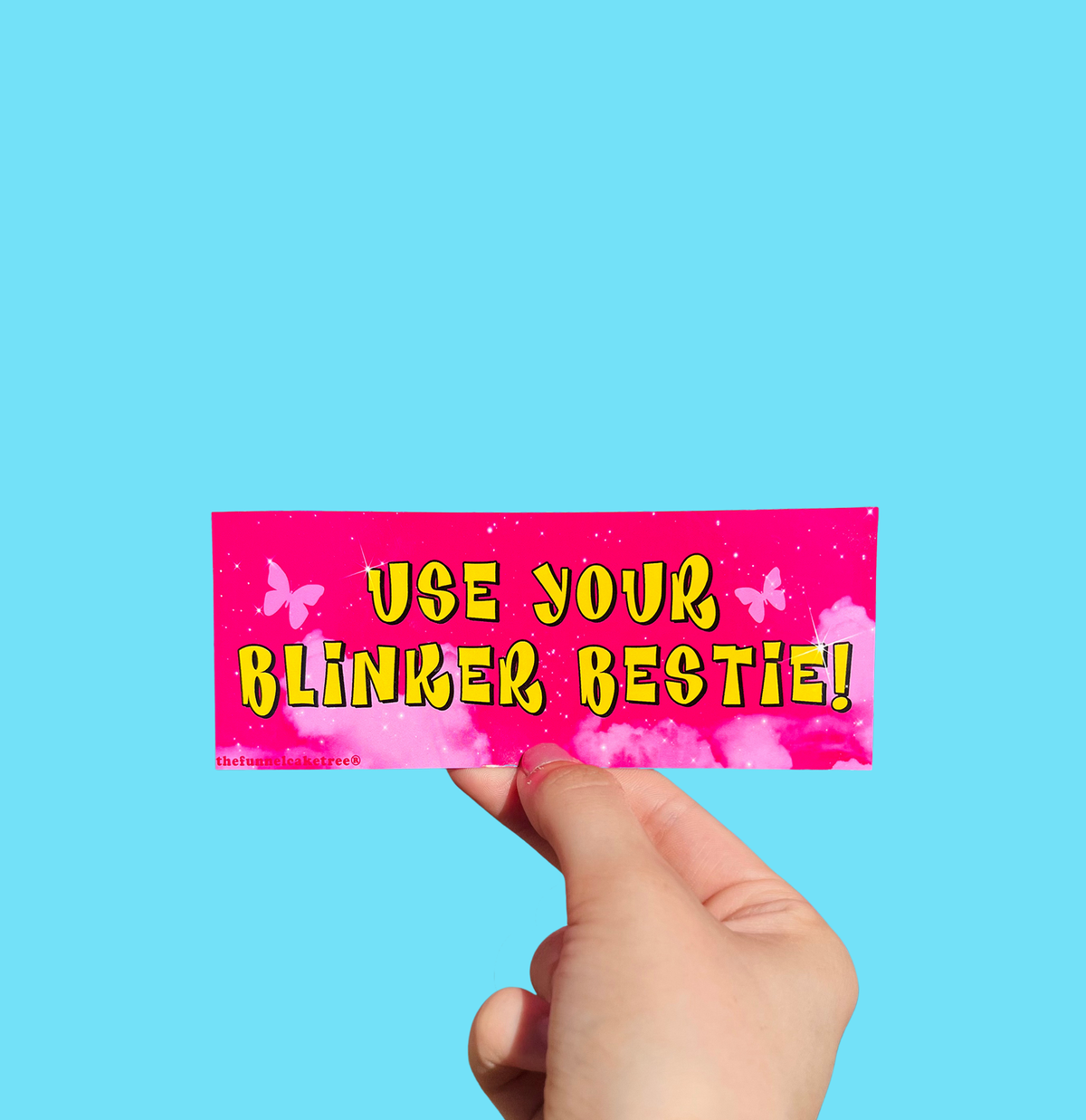 Hand holding a mini bumper sticker reading "use your blinker bestie." On a solid teal background.