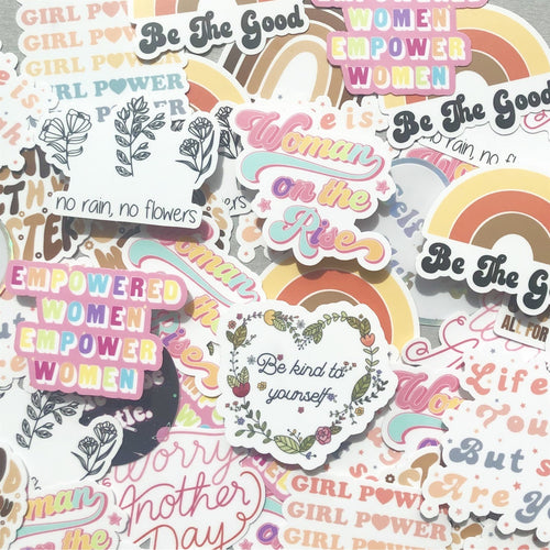 Assorted colorful paper stickers featuring rainbows, flowers, and text like Be the Good and Empowered Women Empower Women.