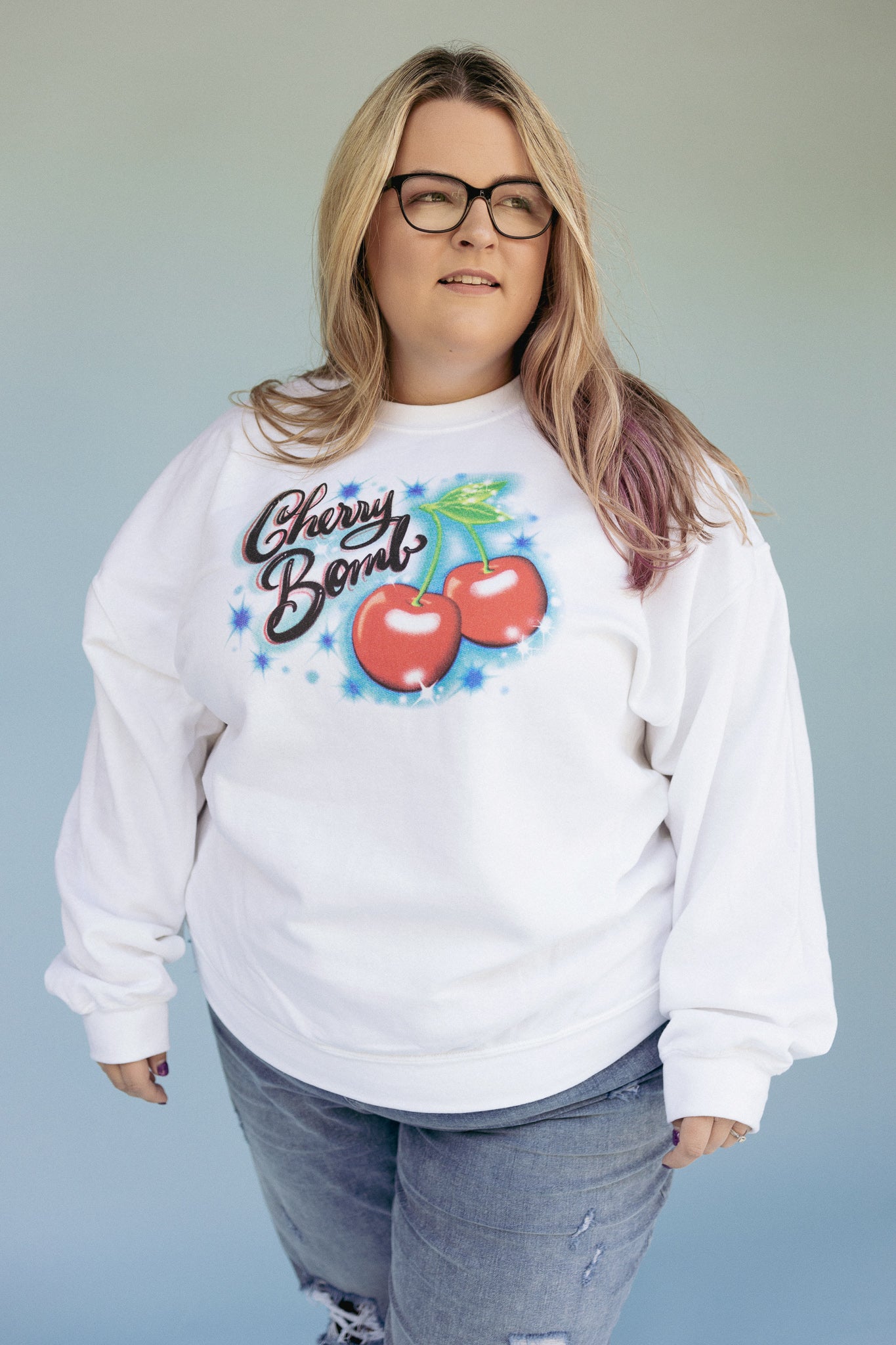 Woman wearing a white crewneck sweatshirt with a Cherry Graphic and the text Cherry Bomb from The Funnel Cake Tree 