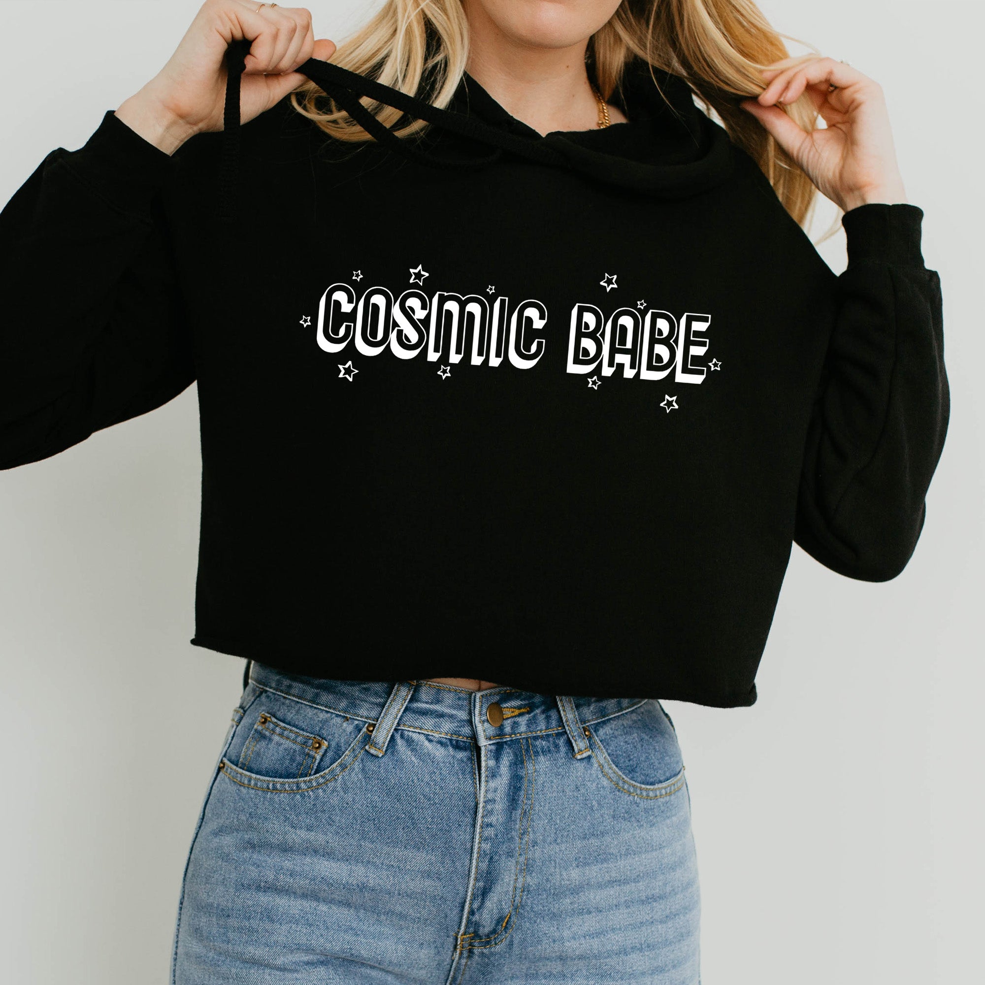 The Funnel Cake Tree “Cosmic Babe” cropped black hoodie with white retro lettering and star accents, styled with high-waisted jeans for a fun and casual cosmic look