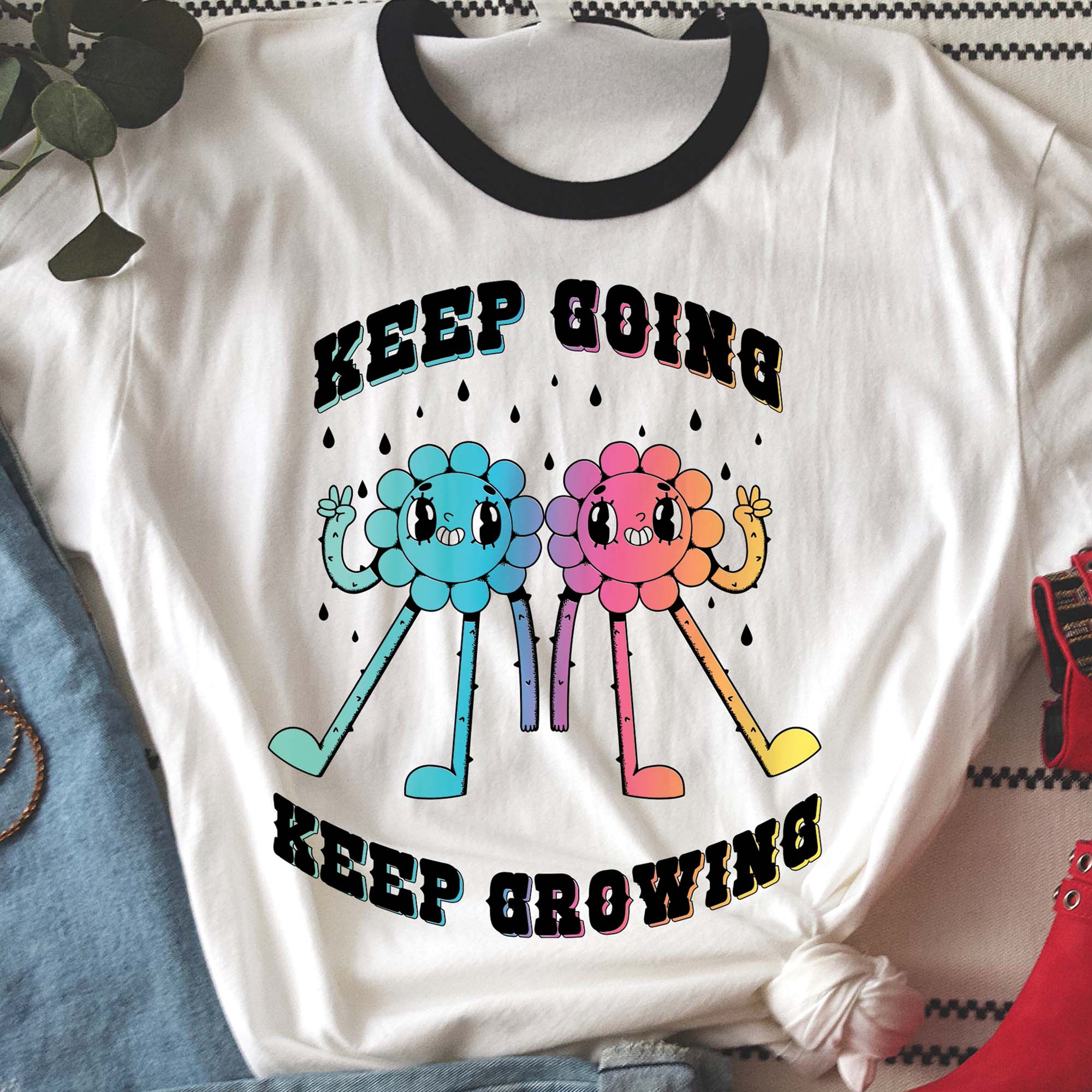 White ringer tee with black collar featuring two colorful cartoon flower characters and the motivational phrase “Keep Going Keep Growing.”