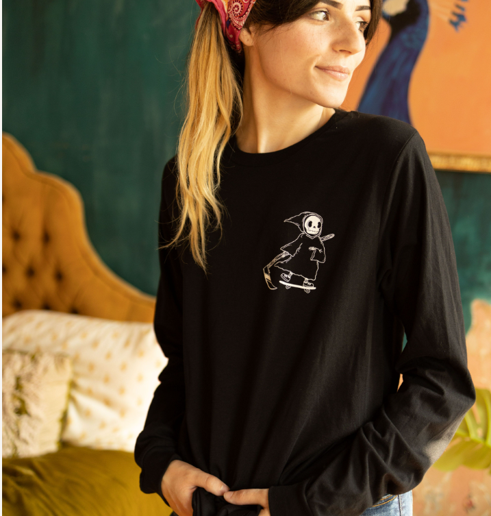 Woman wearing a black long-sleeve shirt with a small graphic of a cute grim reaper riding a skateboard on the chest