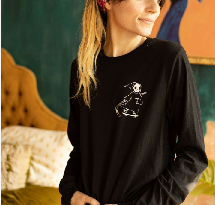 Woman wearing a black long-sleeve shirt with a small graphic of a cute grim reaper riding a skateboard on the chest