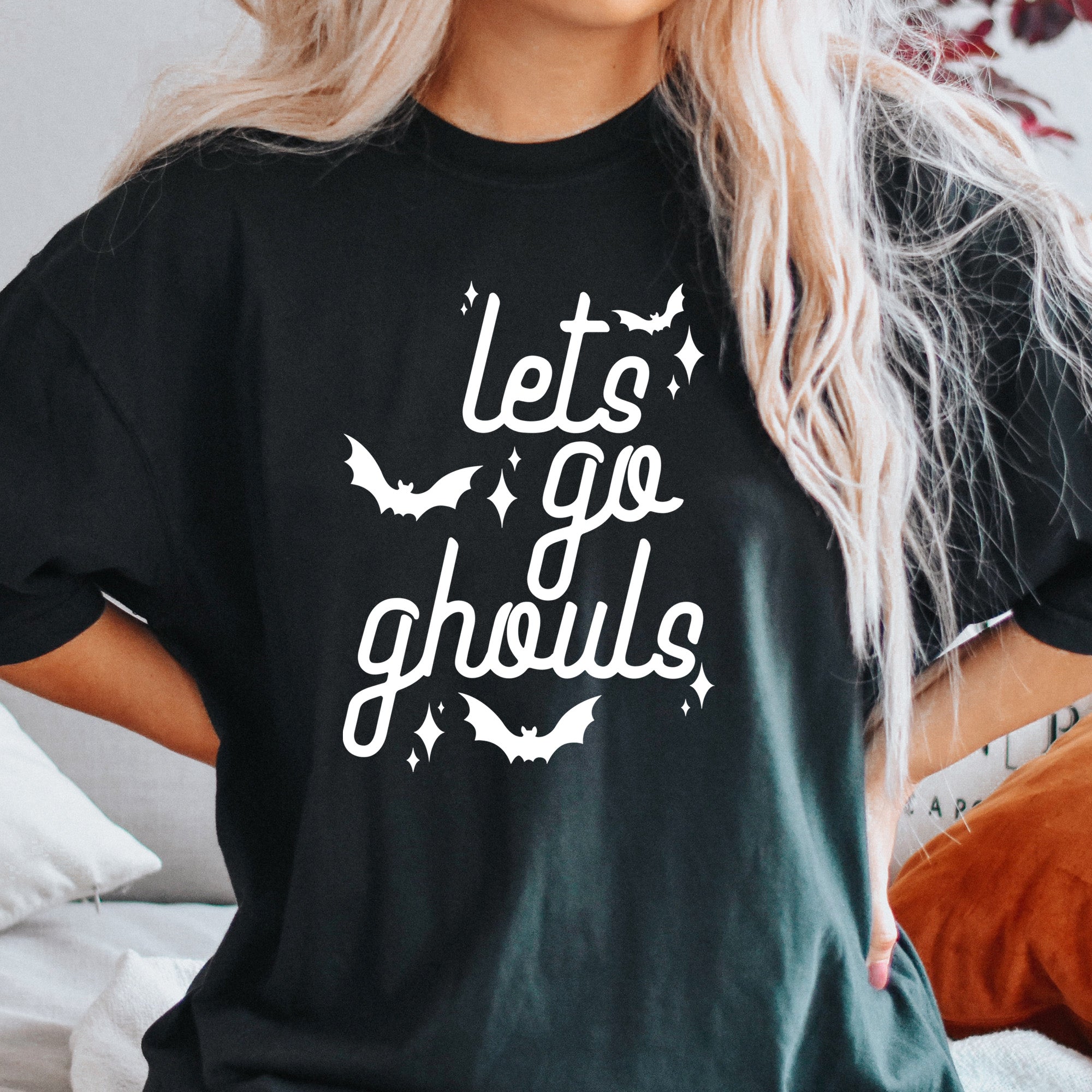 The Funnel Cake Tree “Let’s Go Ghouls” black graphic tee with playful white script lettering, bat illustrations, and sparkle accents — cozy Halloween aesthetic outfit.