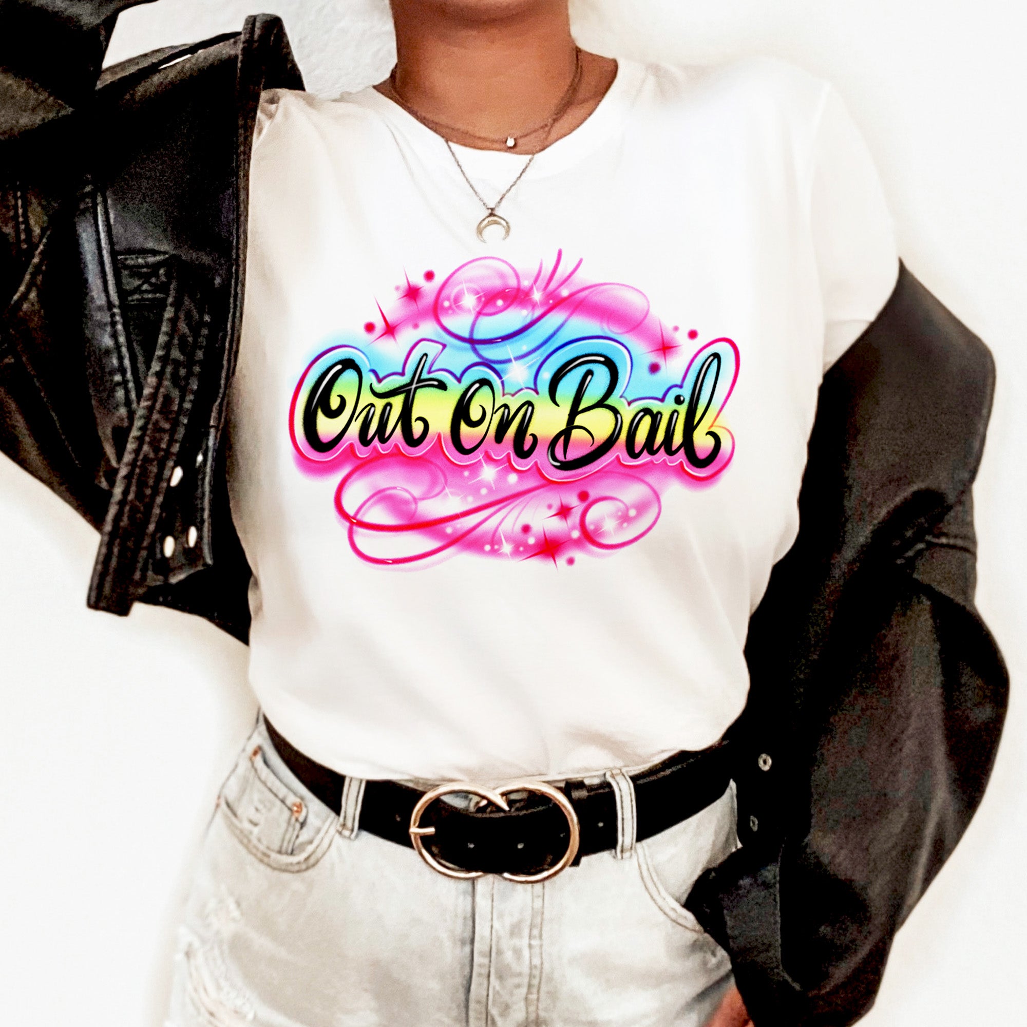 Model wearing a white Out On Bail airbrush-style graphic tee with bold pink, blue, and yellow lettering, styled with a black leather jacket and light denim — The Funnel Cake Tree retro streetwear look.