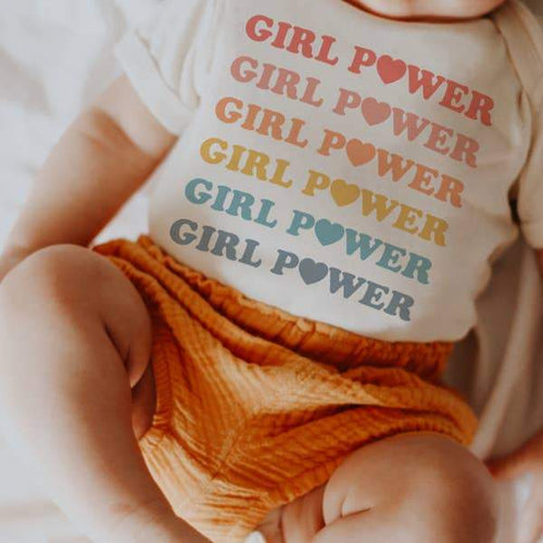 White fabric baby onesie with Girl Power printed in a rainbow of pastel colors and hearts.