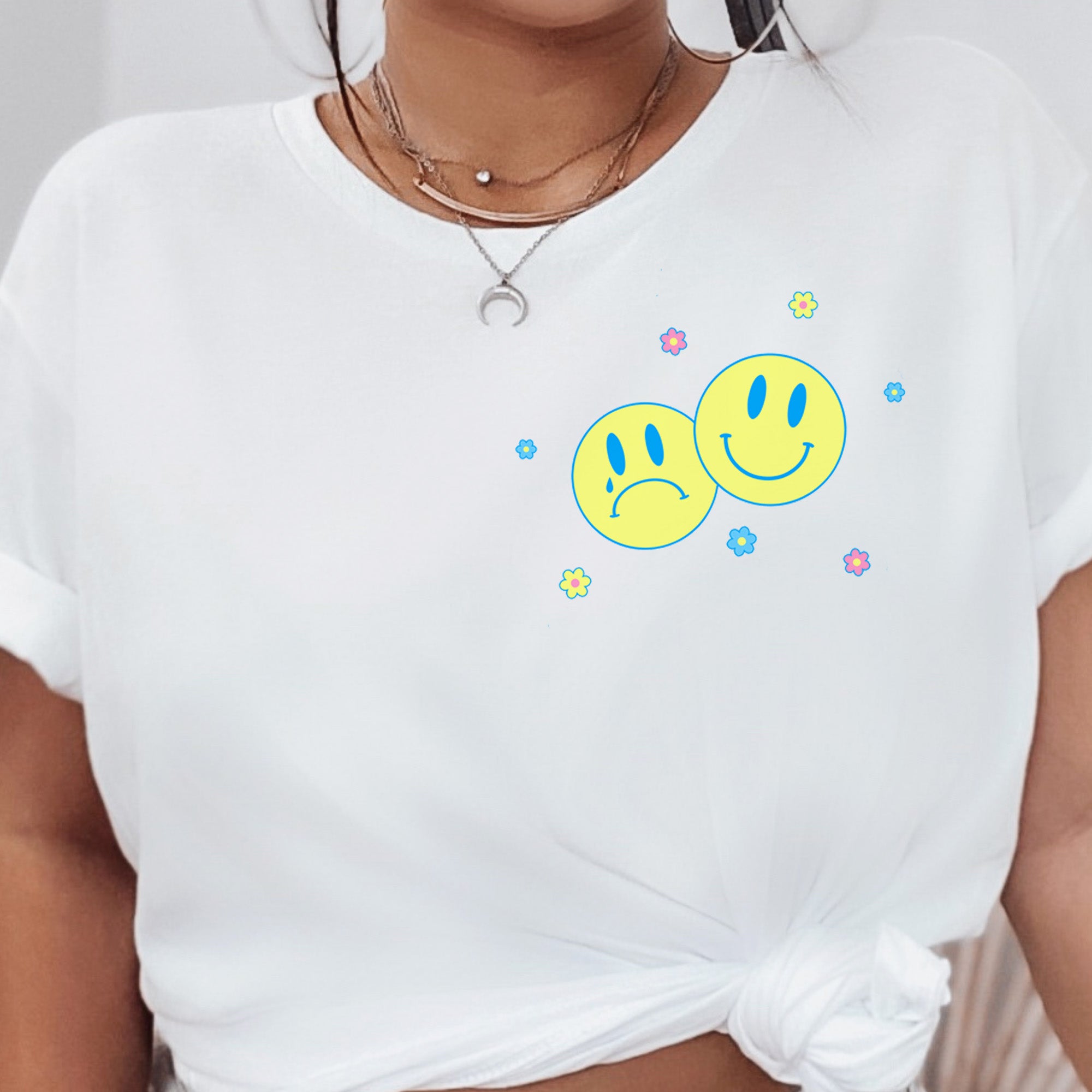 White t-shirt with small front pocket print featuring two yellow smiley faces and pastel flowers – Sometimes Sad Always Rad design – The Funnel Cake Tree.