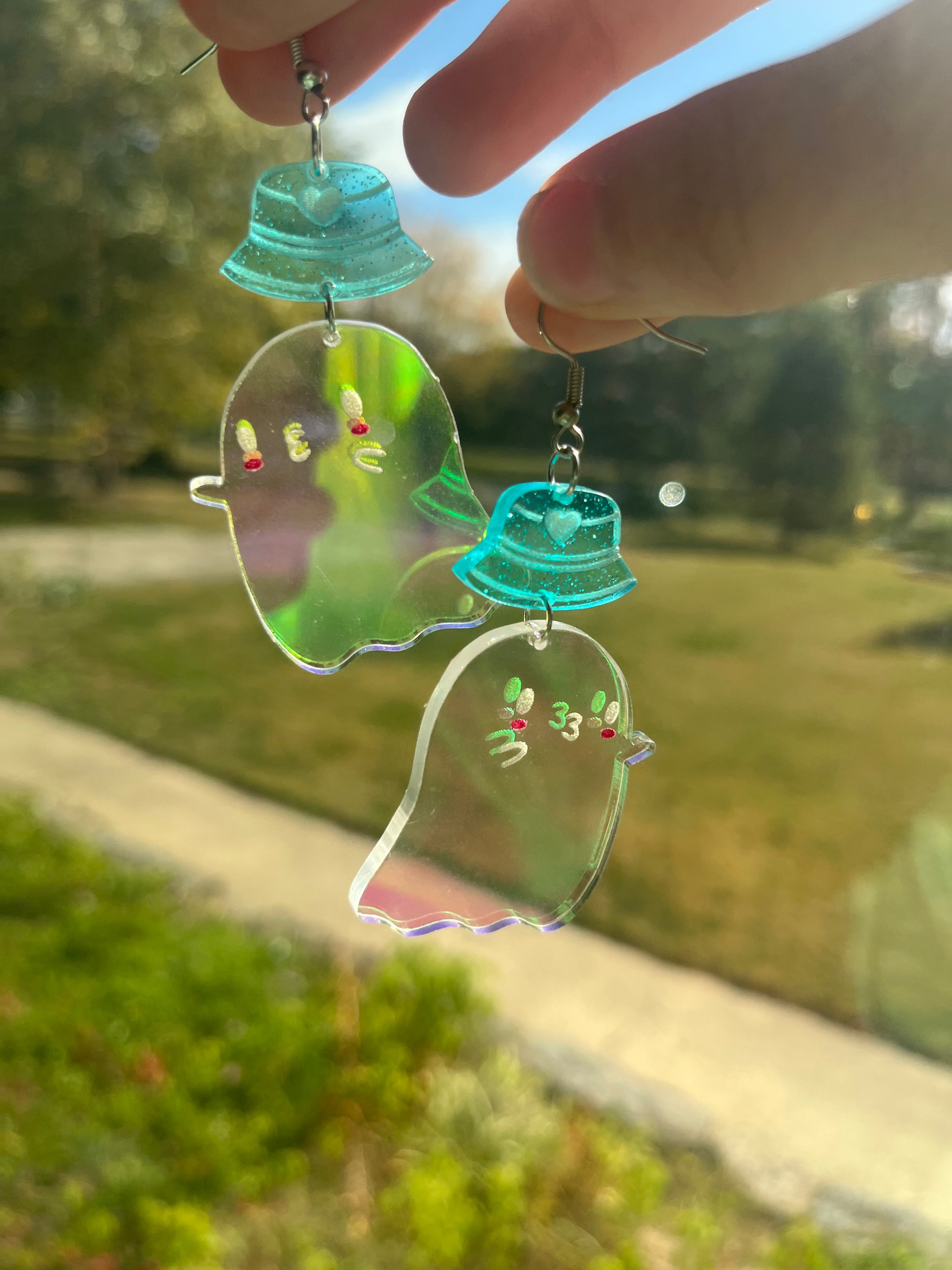 Izy from The Funnel Cake Tree holding ghost dangle earrings in the sun 