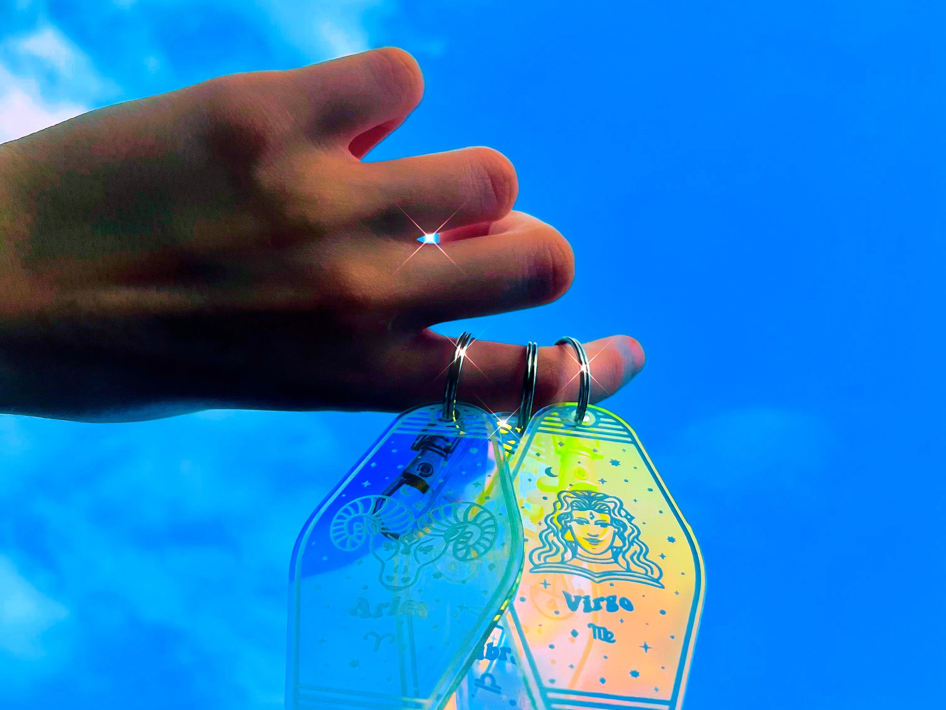 Izy from The Funnel Cake Tree holding 3 of her zodiac acrylic keychains with various zodiac designs engraved on them 