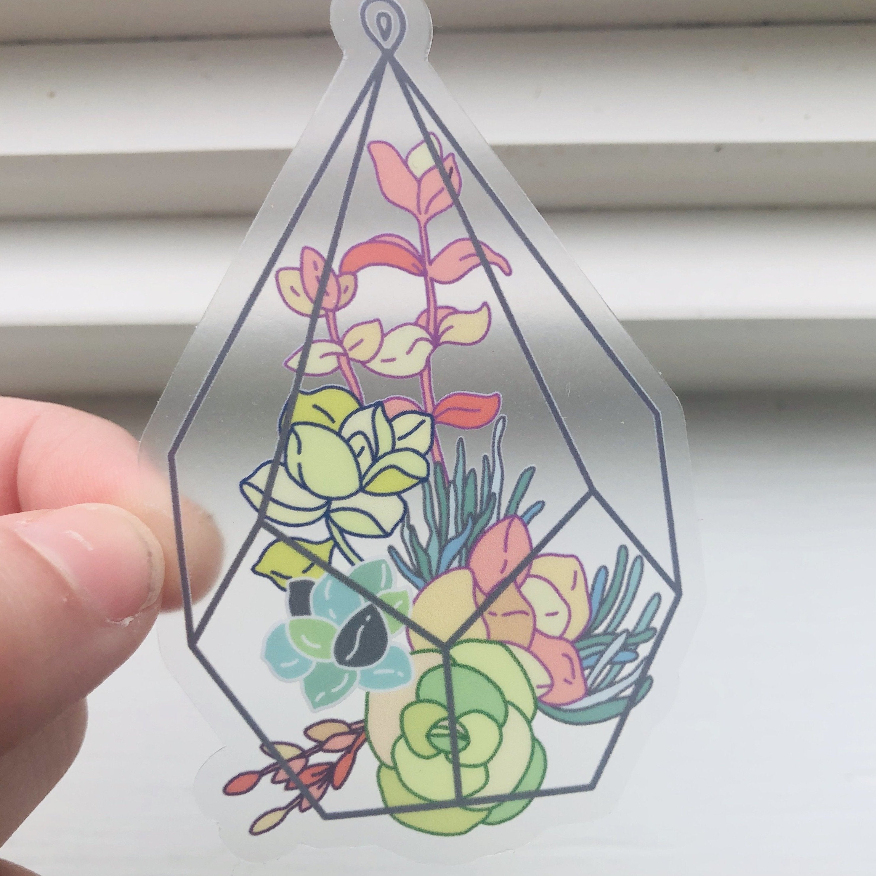 a hand holding a clear succulent filled terrarium sticker on a white background 